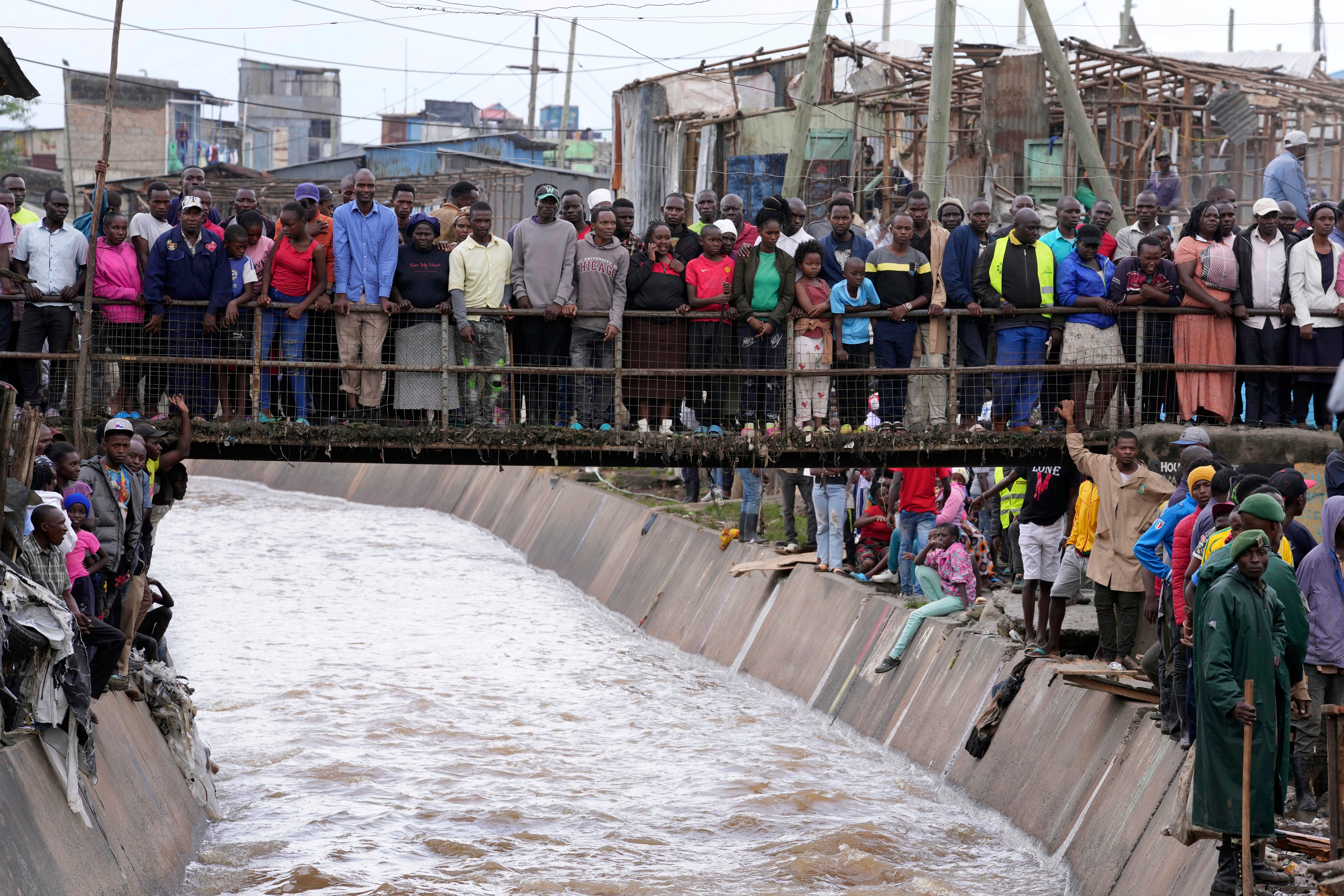 People stand on a bridge, as they watch houses in riparian land being demolished in the Mukuru area of Nairobi, Tuesday, May. 7, 2024. The government ordered the demolition of structures and buildings, illegally constructed along riparian areas. Kenya, along with other parts of East Africa, has been overwhelmed by flooding.