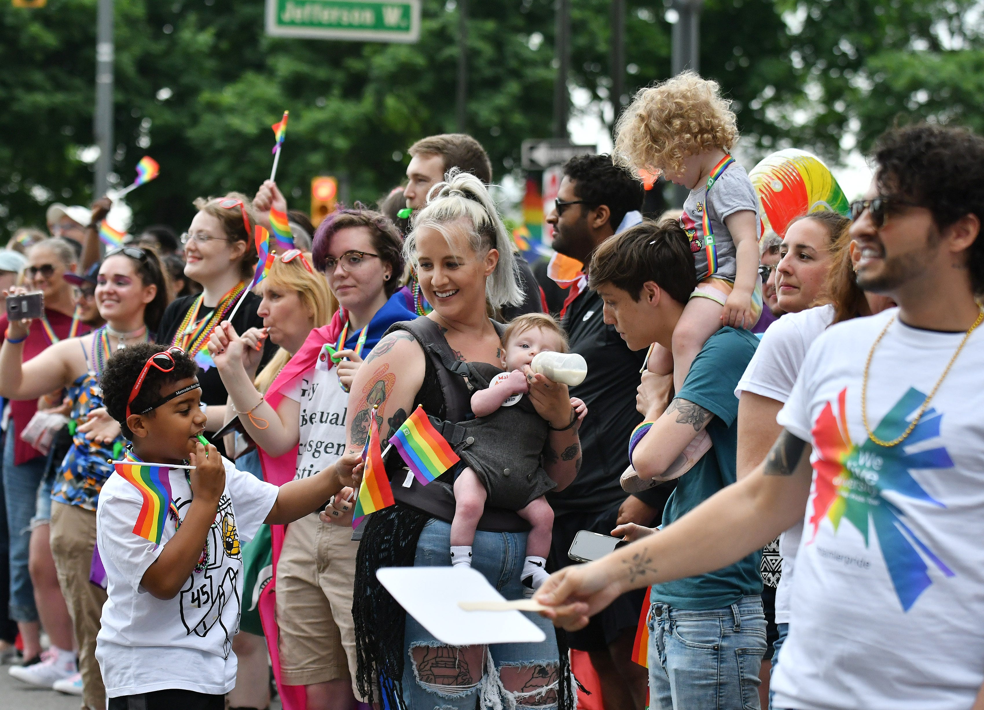 From left, James Shavers, 8, passes a flag to his mom, Allison Gressman, 30, of Warren holding five-month-old Atlas Dunne with Allyssa Palmer, 28, of Taylor with Charlotte Dunne, 1, on her shoulders at the parade.