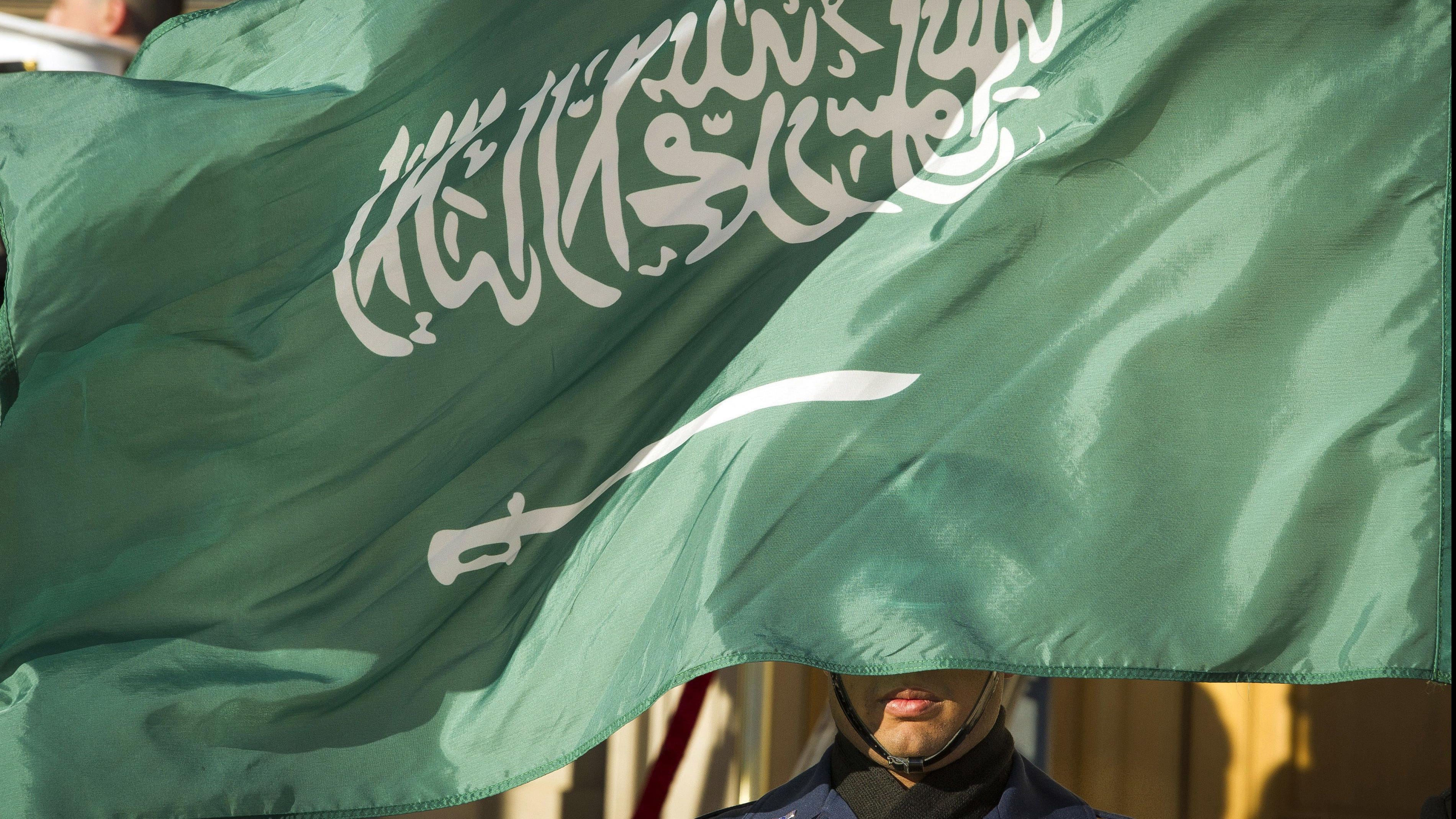 In this March 22, 2018 file photo, an Honor Guard member is covered by the flag of Saudi Arabia.