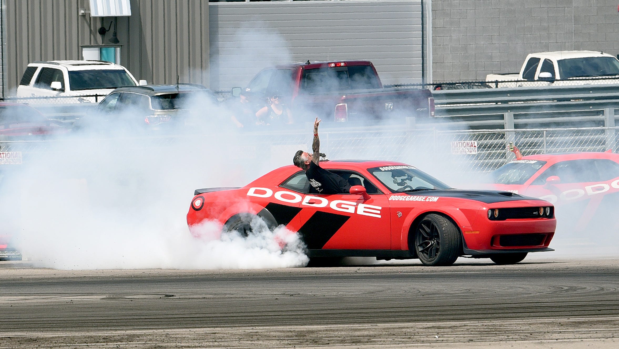 A passenger celebrates with a fist pump as the a Dodge Challenger hellcat performs a burnout at the Dodge drift rides demonstration.