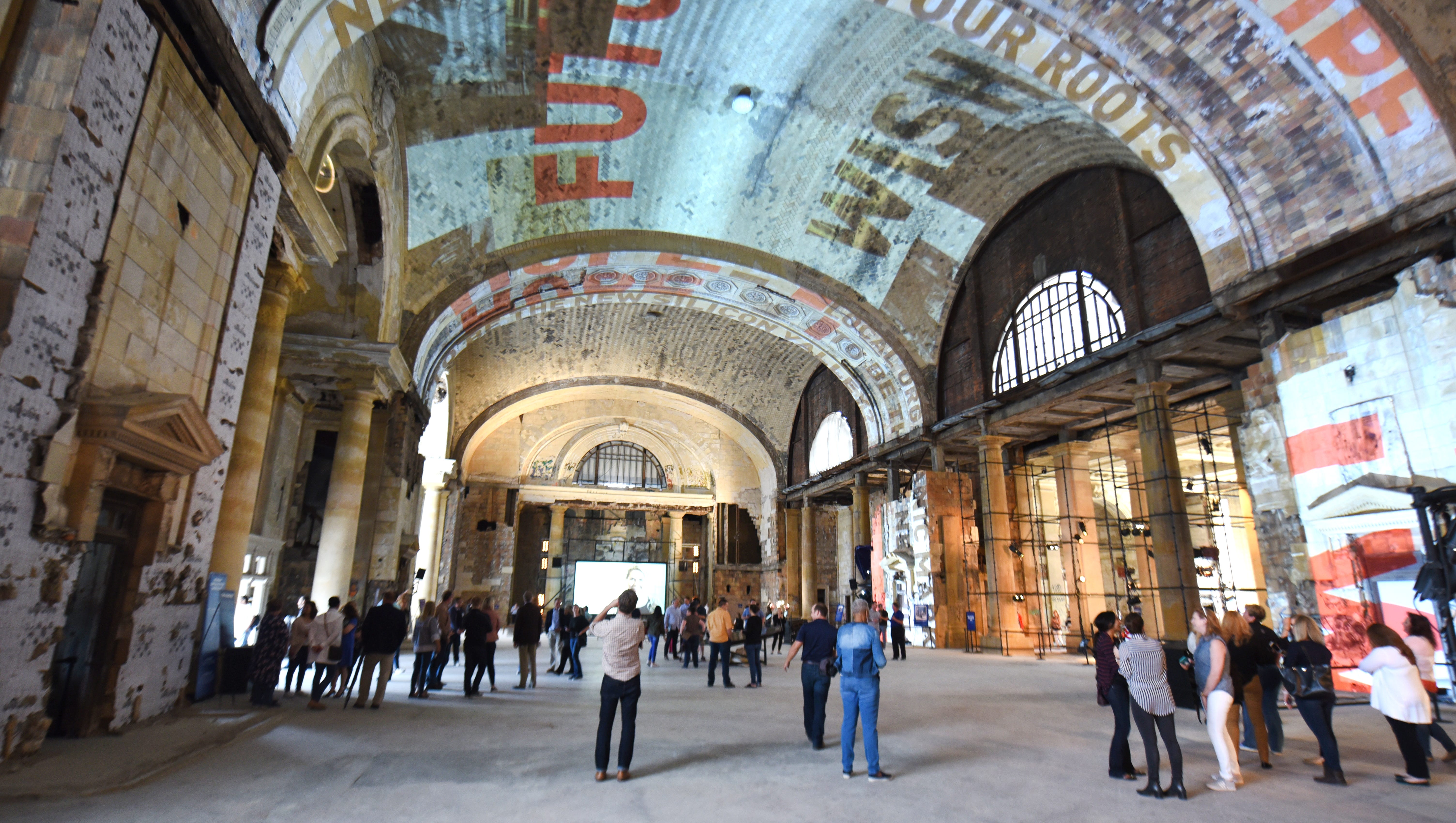 People gather in the grand hall of the Michigan Central Train Depot, where messages are projected on the ceiling.