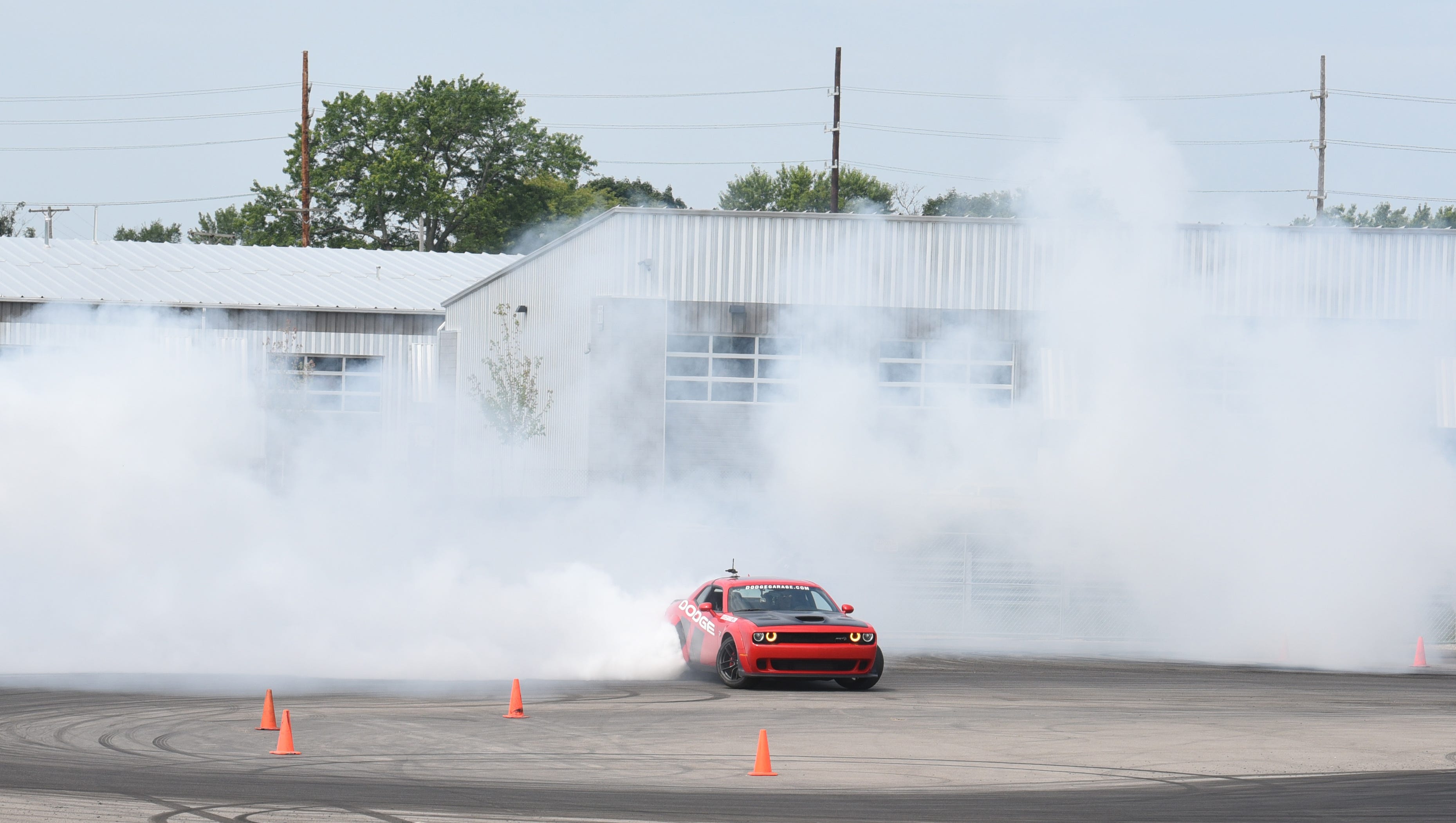 A Dodge Challenger hellcat is surrounded by white smoke during a  burnout.