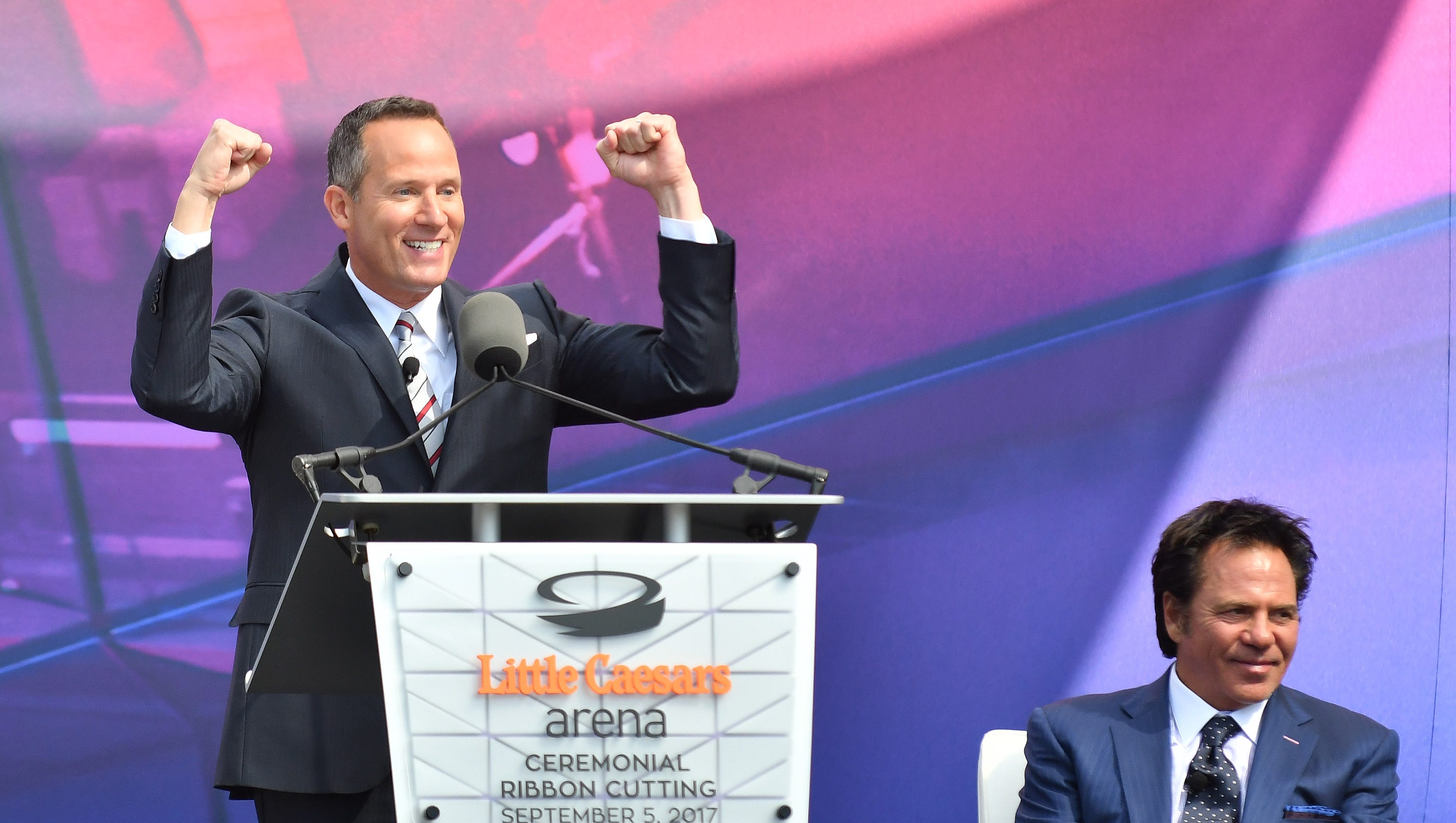 Chris Ilitch immitates his father, Mike Ilitch, pumping two fists in the air during the ribbon cutting ceremony for Little Caesars Arena in Detroit on September 5, 2017.