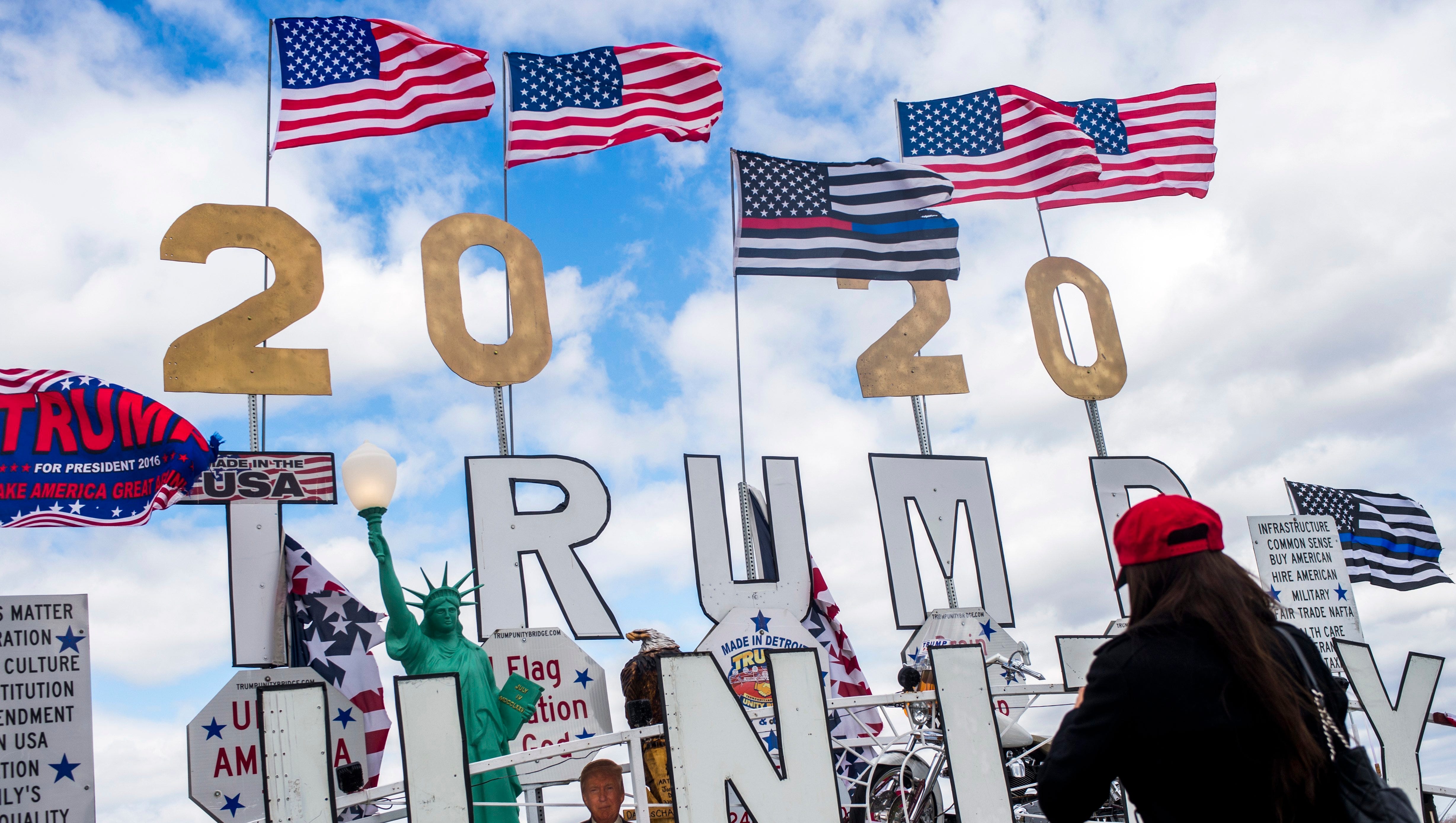Flags fly high above the Trump Unity Bridge, a mobile float parked outside of the rally's entrance, as thousands of supporters of President Donald J. Trump wait in line Saturday in Washington Township.
