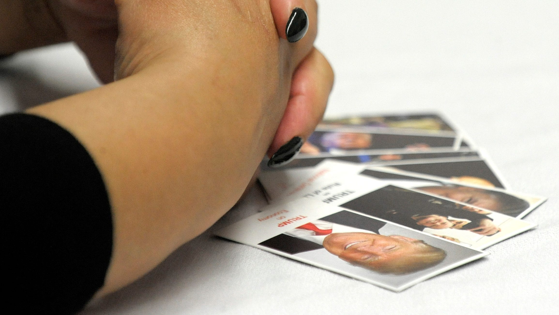 A woman folds her hands as she listens to Donald Trump, Jr. with pictured cards on the table, including, a card of Donald Trump.