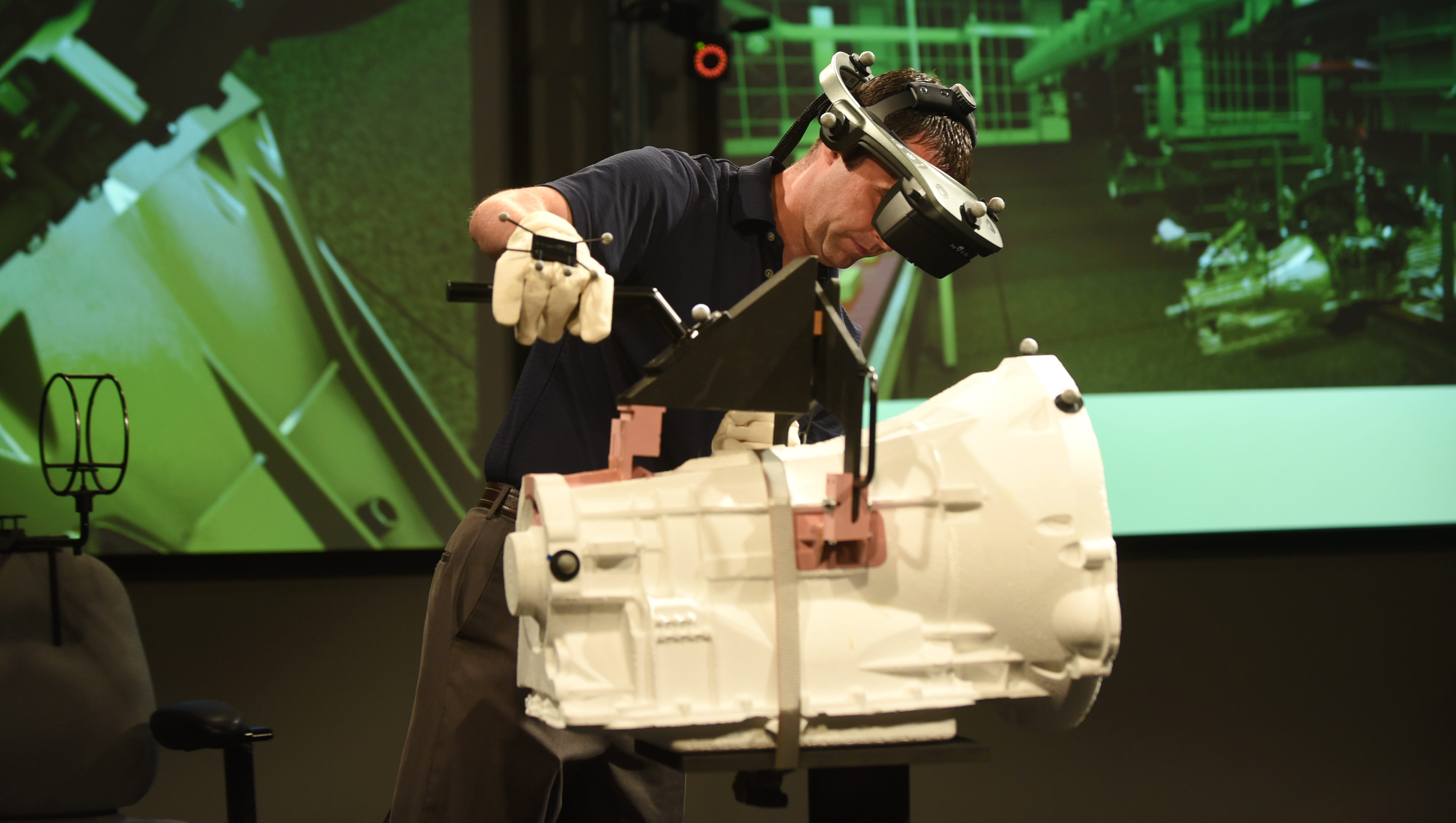 Rob McLean wears immersive virtual reality headgear as he demonstrates the marriage of a transmission to engine.