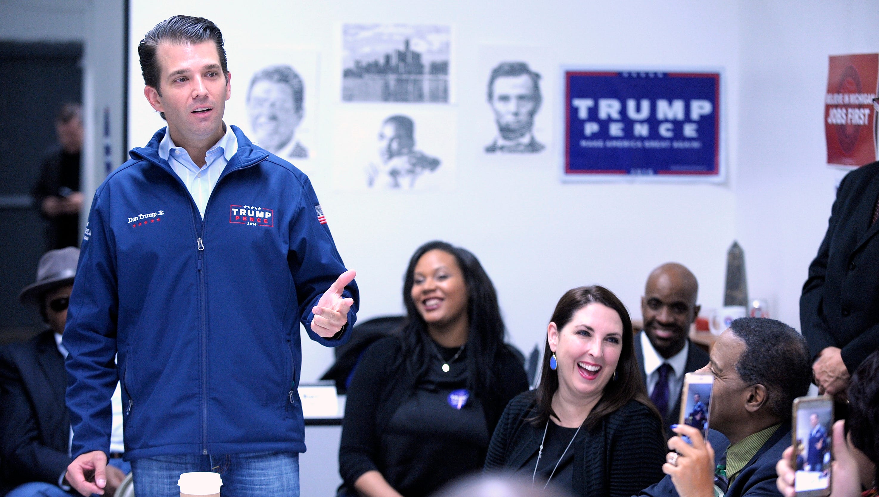 Donald Trump Jr. stands as he addresses the attendees as Ronna Romney McDaniel, center-right, Michigan Republican Party chairman, shares a laugh with others.