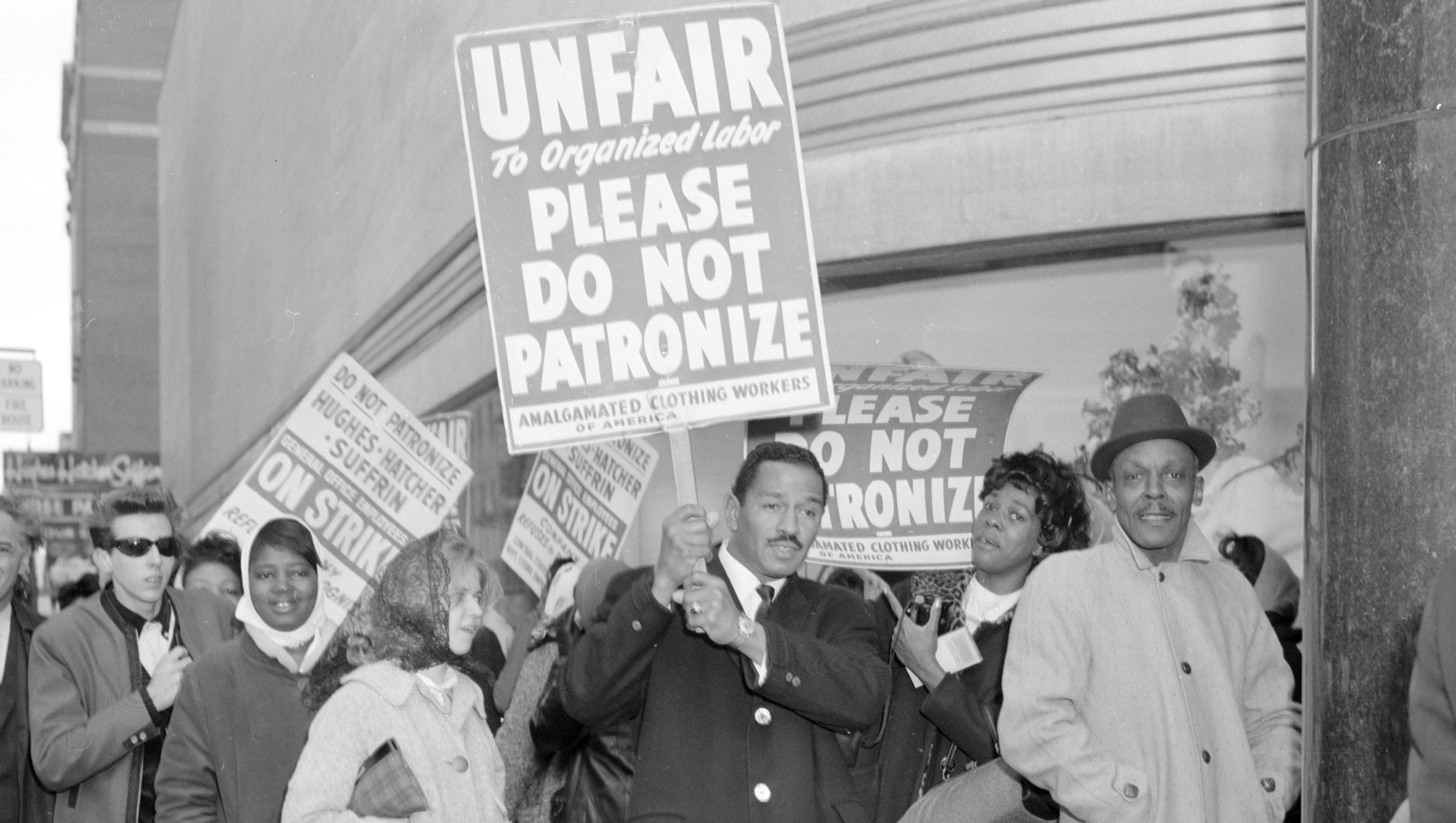 Conyers carries a picket sign during a strike at a Hughes-Hatcher-Suffrin clothing store in 1965.