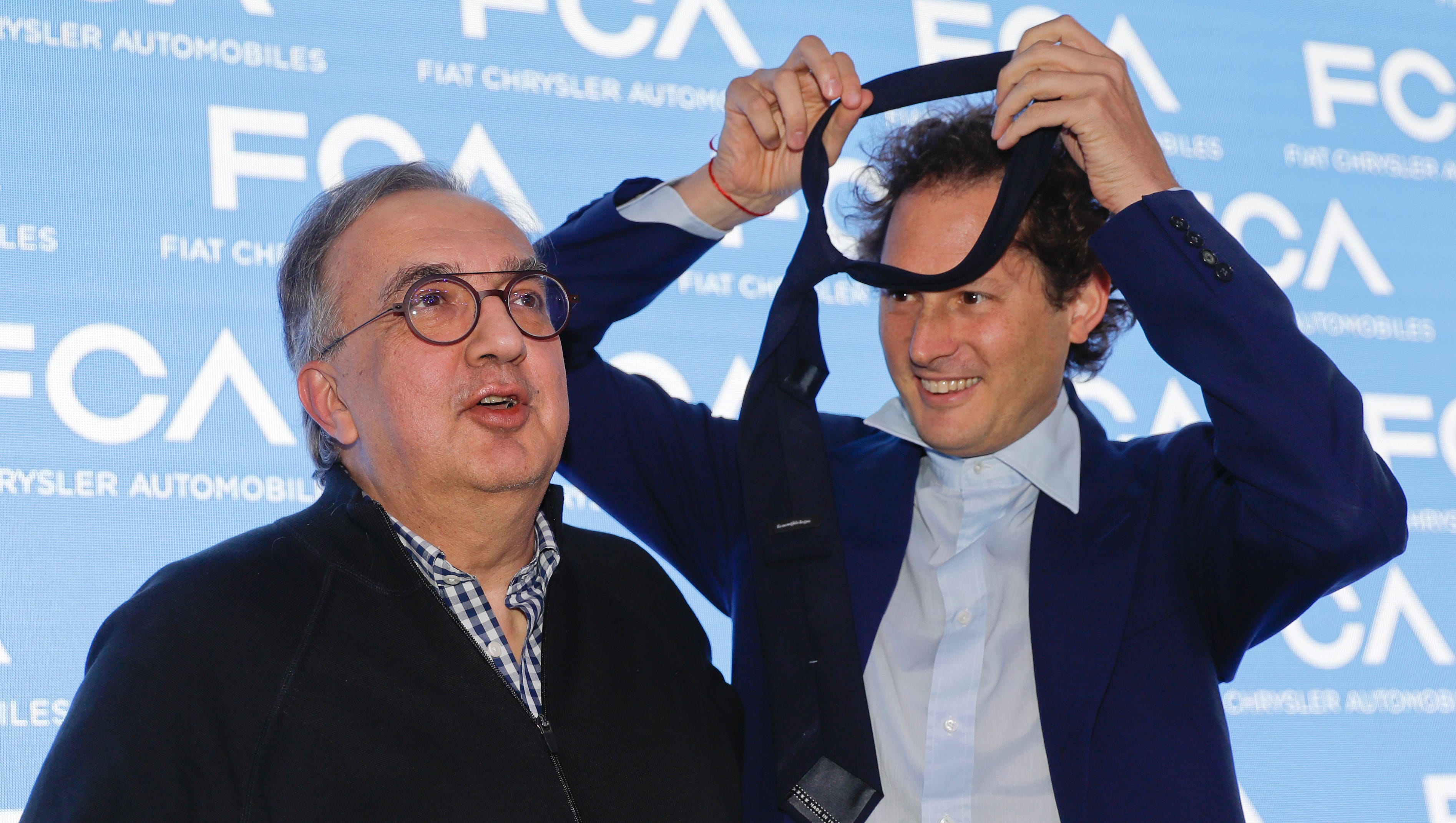 John Elkann, president of the FCA Italy group, right, gives his necktie to the famously tie-less Fiat Chrysler CEO Sergio Marchionne prior to a press conference in Balocco, Italy, Friday, June 1, 2018. In his last big presentation as CEO of Fiat Chrysler before retiring, Marchionne announced a big investment push to make more electrified cars, while acknowledging that traditional engines will continue to dominate production for some time.