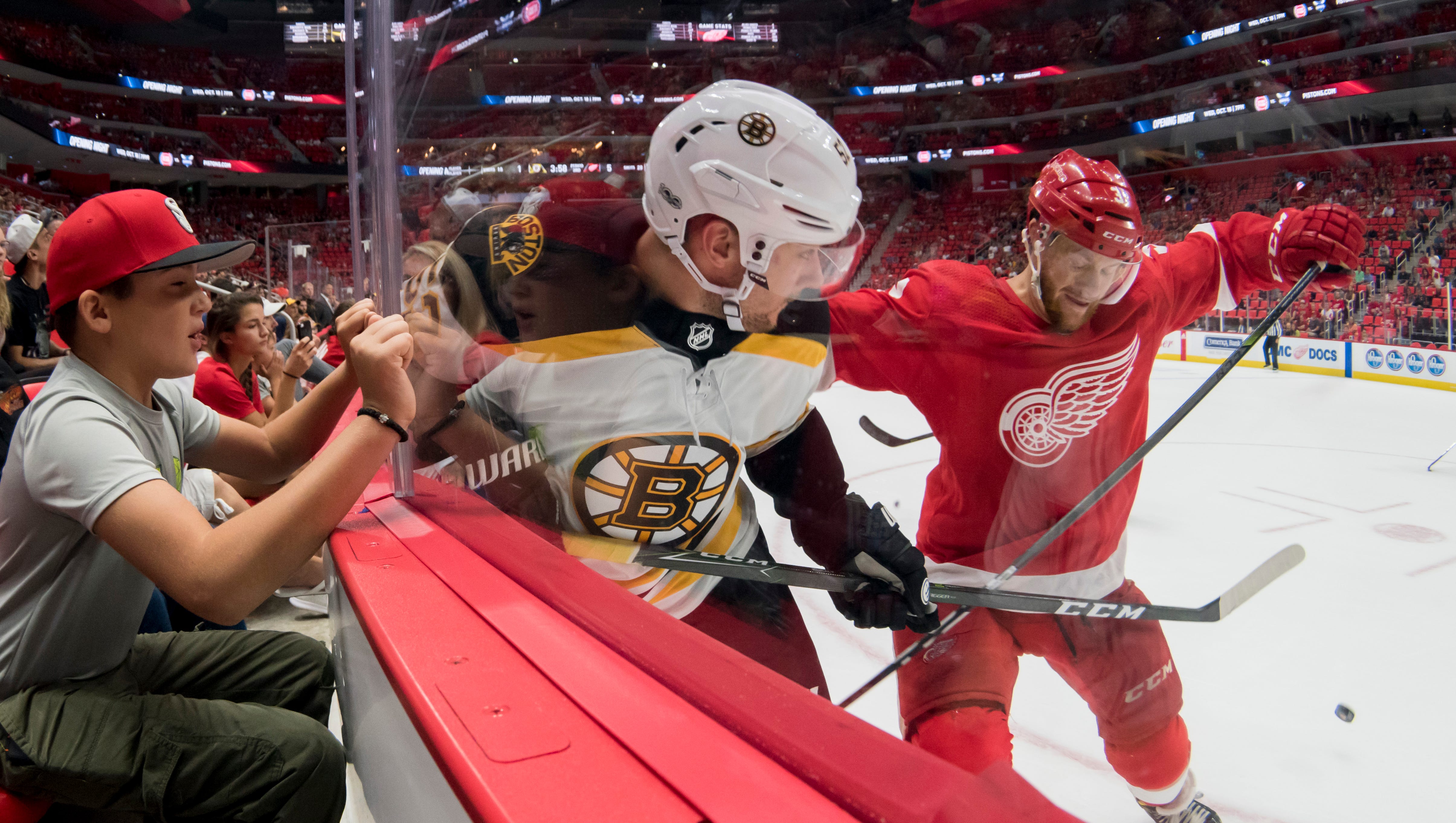 Boston center Sean Kuraly and Detroit defenseman Nick Jensen collide in front of eleven-year-old Miki Simasao, of St. Clair Shores during the first sporting event, a Red Wings preseason hockey game, at Little Caesars Arena, in Detroit, September 23, 2017.