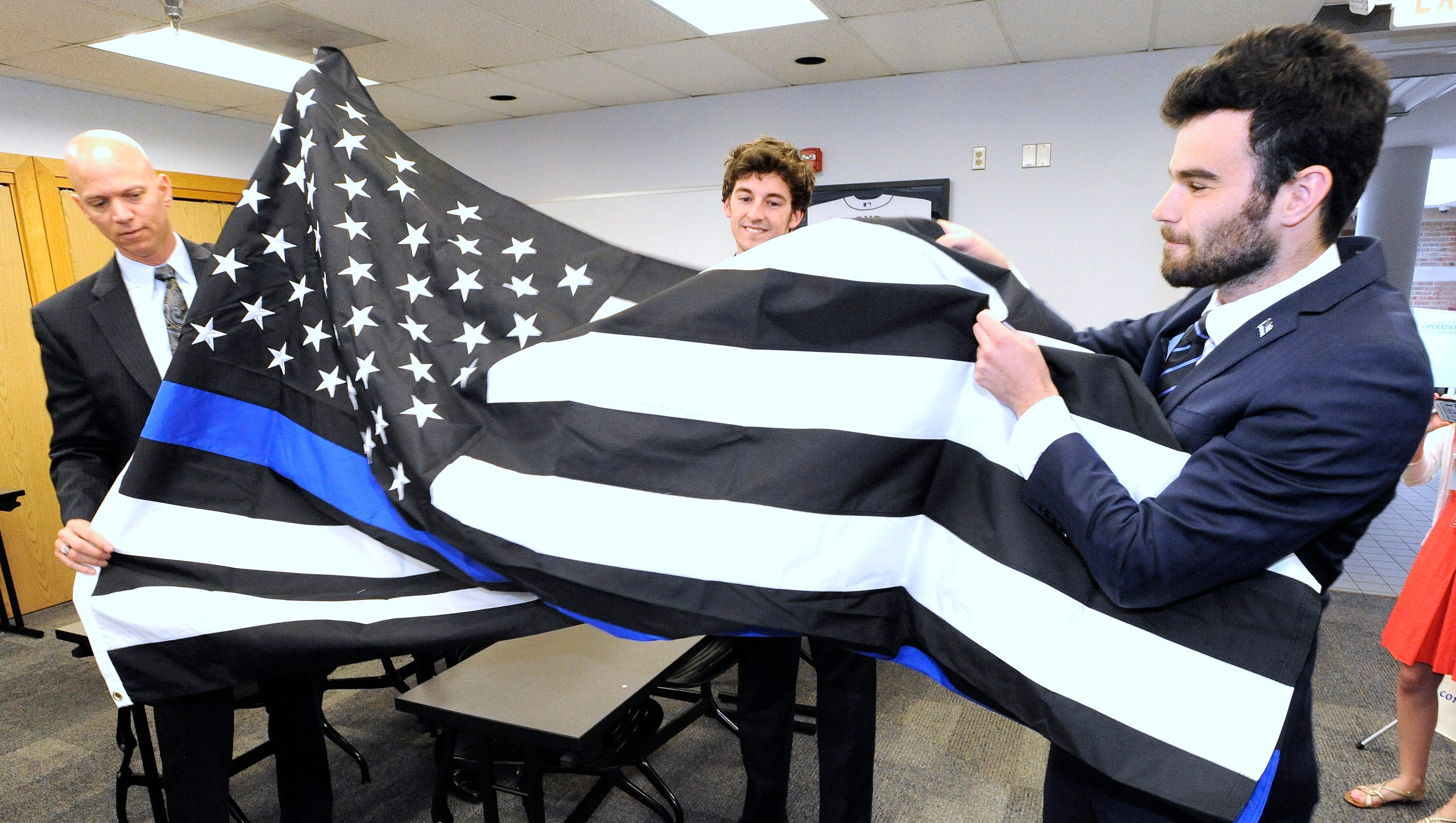 From left, West Bloomfield Twp. deputy chief Curt Lawson, Thin Blue Line vice president Pete Forhan and founder and president Andrew Jacob unfurl this 5-foot by 8-foot Thin Blue Line flag that Jacob presents to Lawson, for the department.