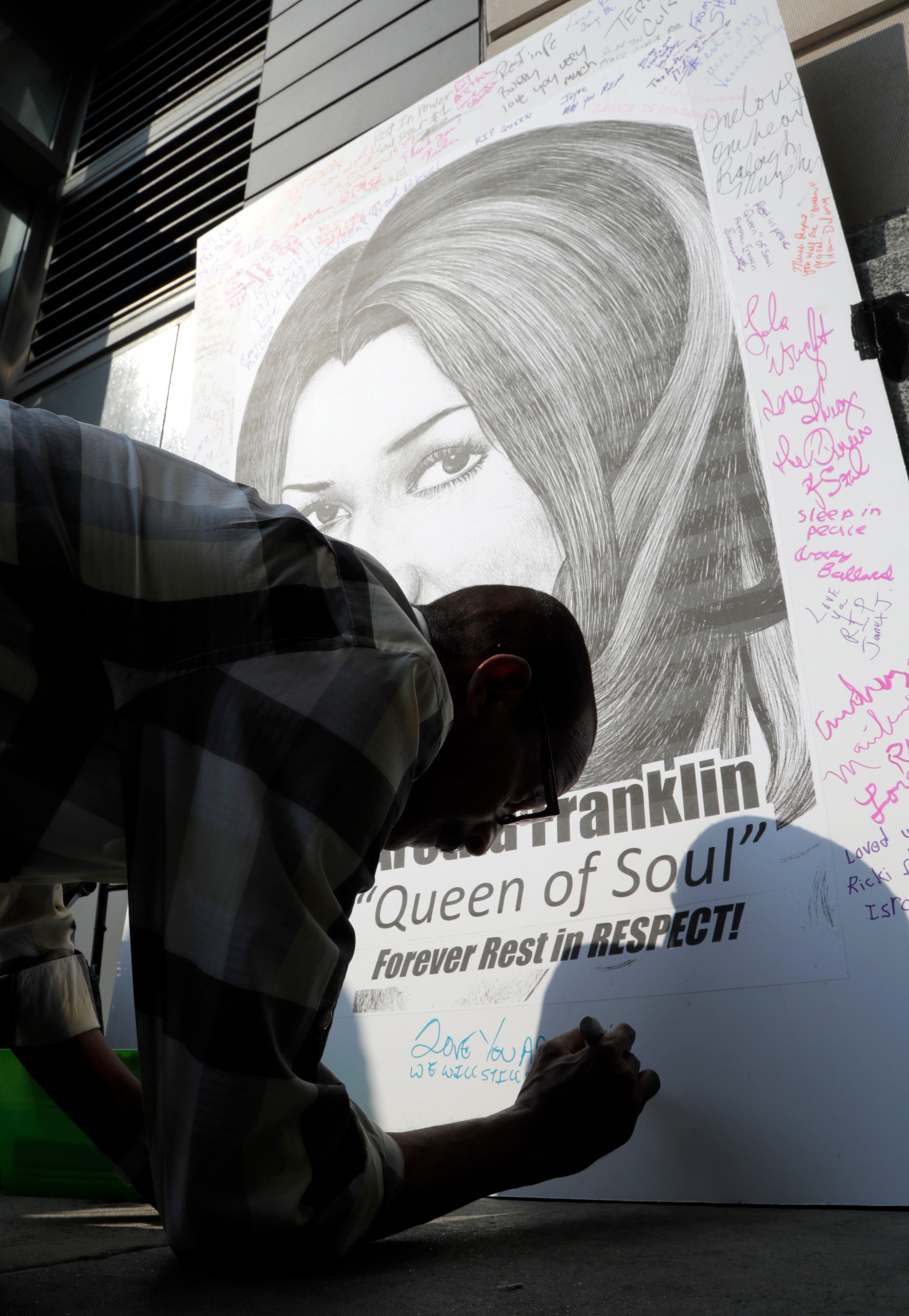 A man writes a message on a large portrait of singer Aretha Franklin outside the Apollo Theater in New York City, Thursday.
