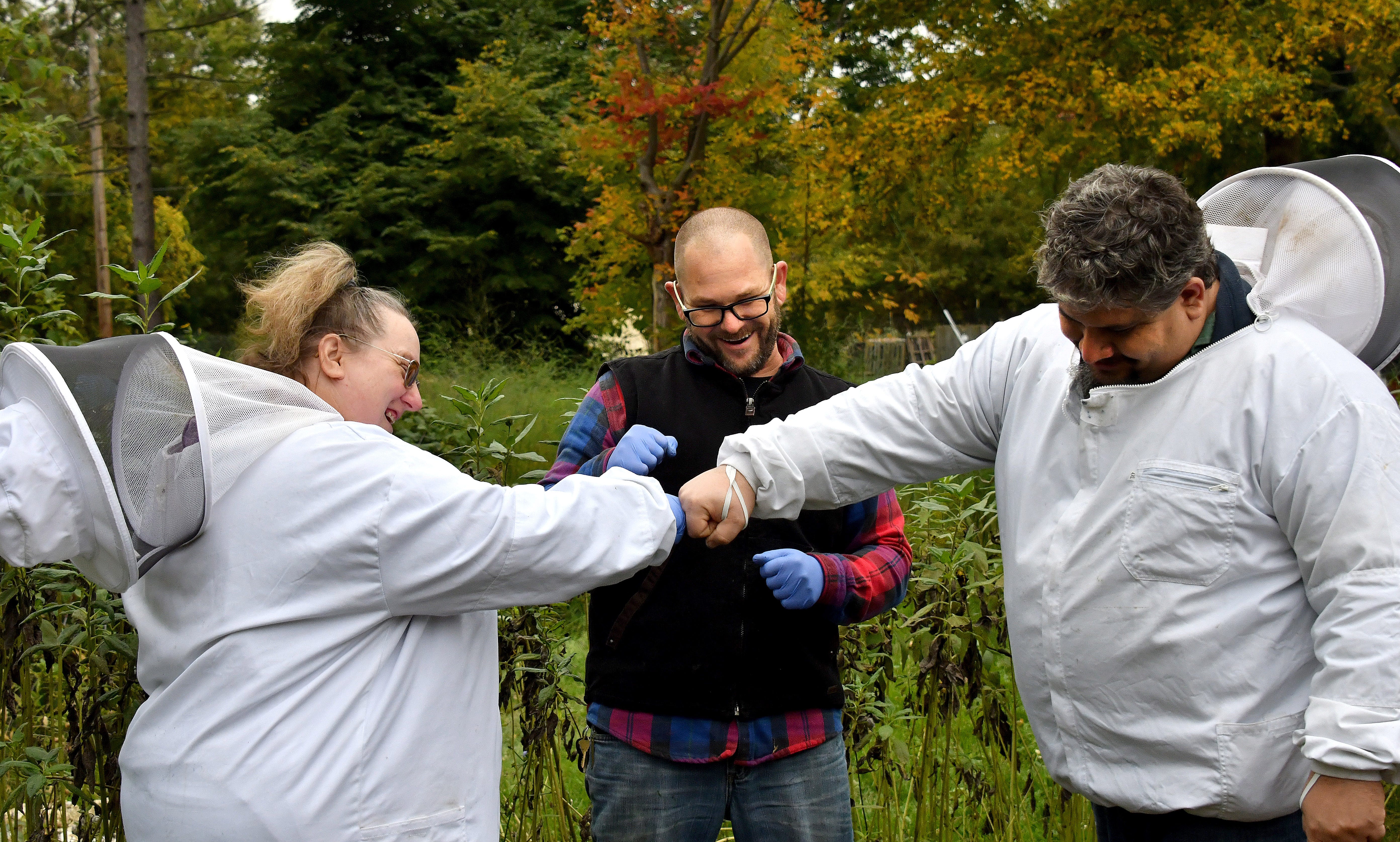 Adam Ingrao (center) jokes and fist-bumps with Marine veteran Tom Kusar (right) and US Army veteran Marie Jaegers in an urban garden on Oct 12, 2018 in Lansing. The fist bump came when Tom Kusar was told he was doing something right with his beekeeping program at home.