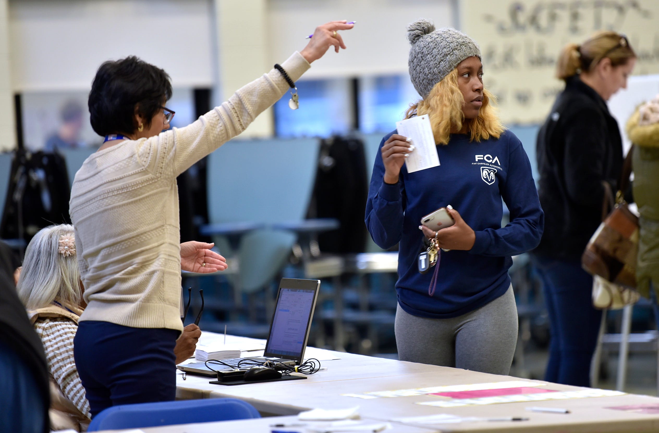 A precinct worker instructs Samara Brame, right, of Macomb Township where to get her ballot in the cafeteria at Ojibwa Elementary School. Brame is a UAW Local 140 member who builds Fiat Chrysler automobiles.