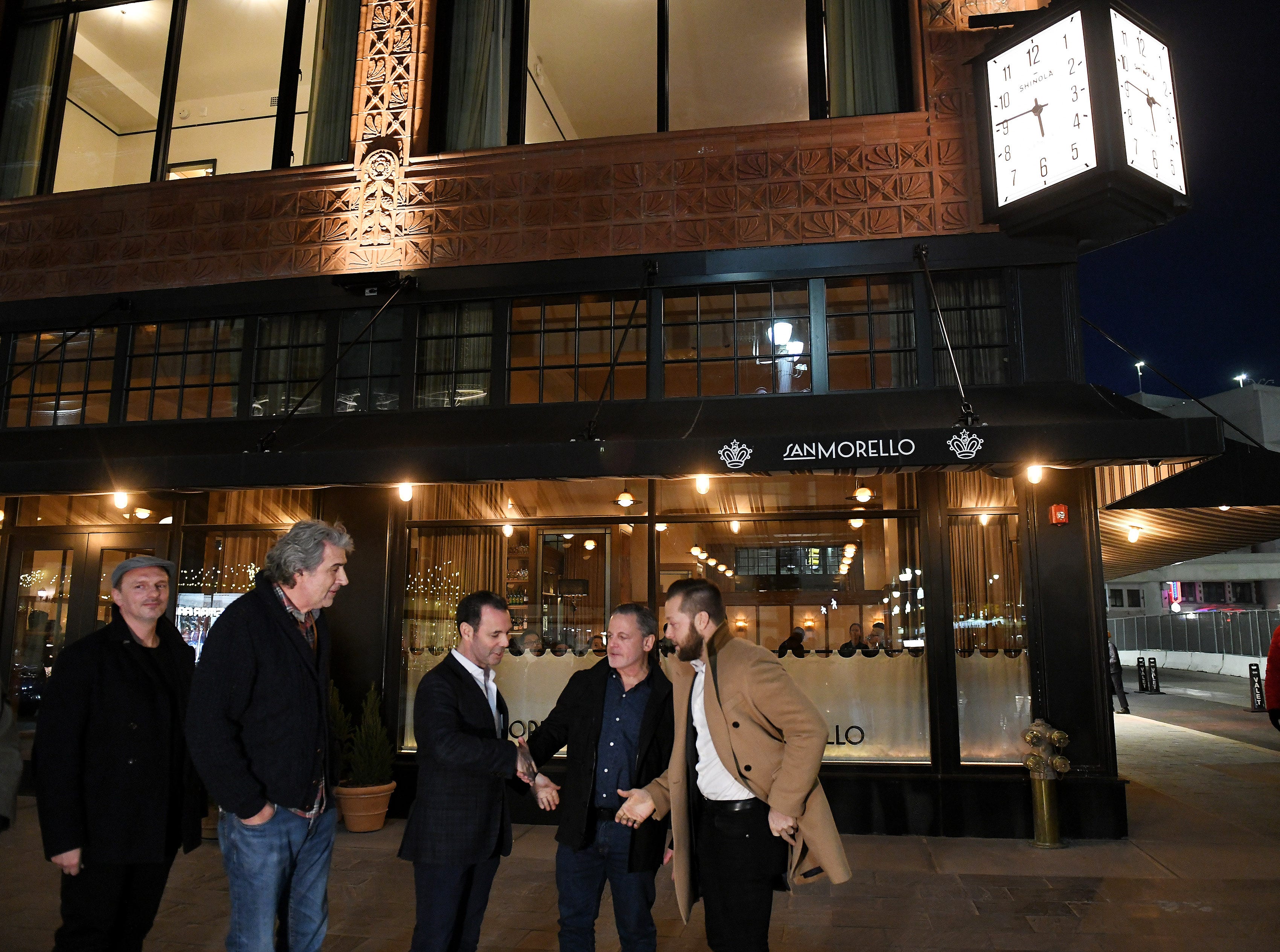 After the exterior lights are turned on, Dan Gilbert, second from right, shakes hands with Bedrock chairman Jim Ketai with Shinola founder Tom Kartsotis, second from left.
