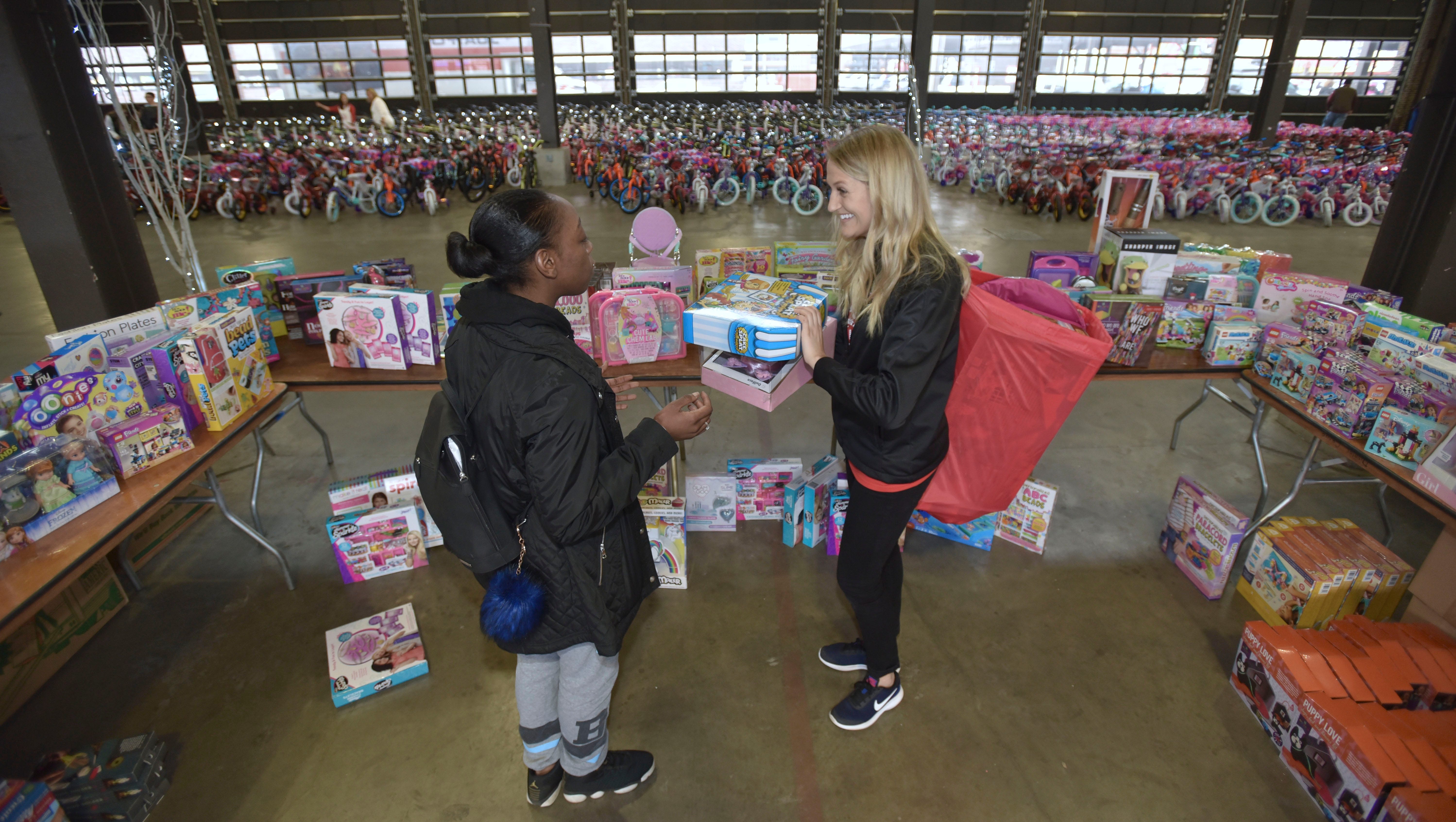 Pistons Community and Social Responsibility Coordinator Chelsey Oeffler, right, carries a bag full of presents as she helps Brenda Jones, left, of Hamtramck shop for her three daughters.