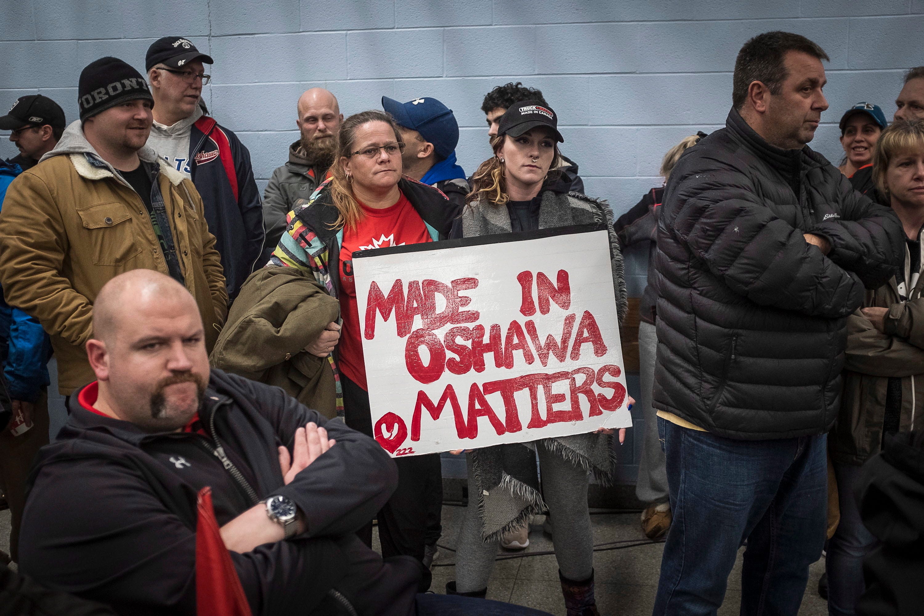 Laurie Nickel, center left, and her daughter Stephanie hold a sign during a UNIFOR union meeting between the workers of Oshawa's General Motors plant with Jerry Dias, president of UNIFOR, at the plant in Oshawa, Ontario, Monday, Nov. 26, 2018. General Motors will cut up to 14,000 workers in North America and put five plants up for possible closure as it abandons many of its car models and restructures to focus more on autonomous and electric vehicles, the automaker announced Monday. (Eduardo Lima/The Canadian Press via AP)