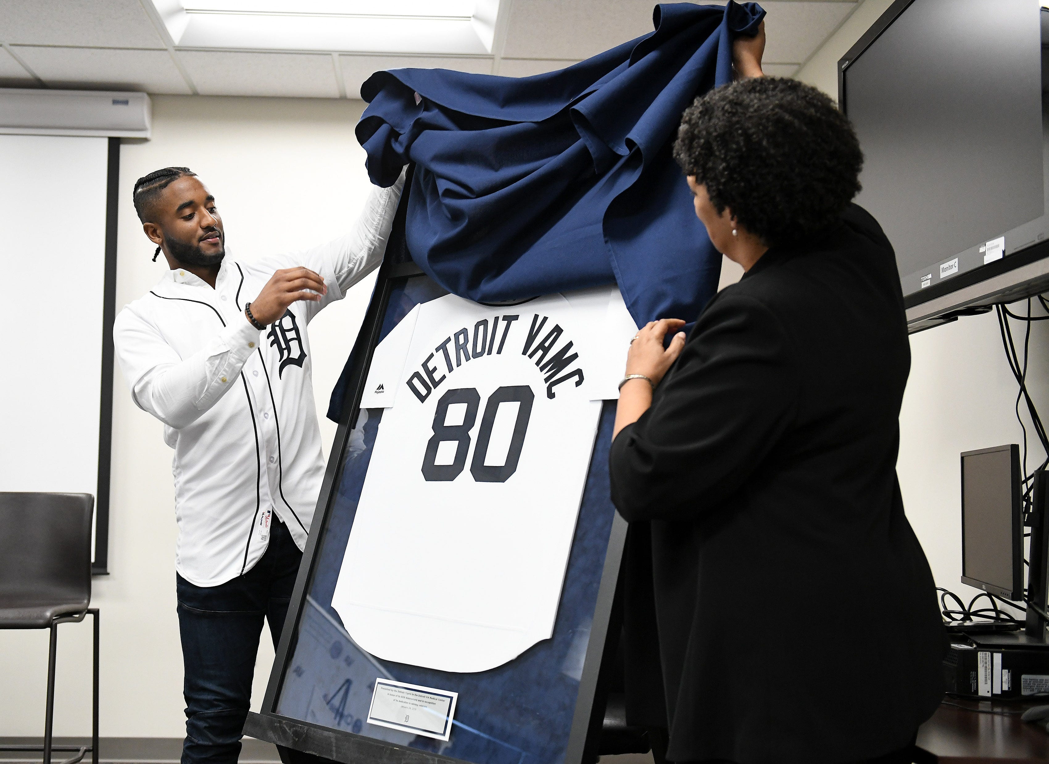 Tigers' Niko Goodrum, left, and John D. Dingell VA Medical Center director Pamela J. Reeves, MD, unveil a special jersey celebrating 80 years of service by the Detroit VA Medical Center during a stop on the 2019 Detroit Tigers Winter Caravan at the John D. Dingell VA Medical Center in Detroit on Jan. 24, 2019.