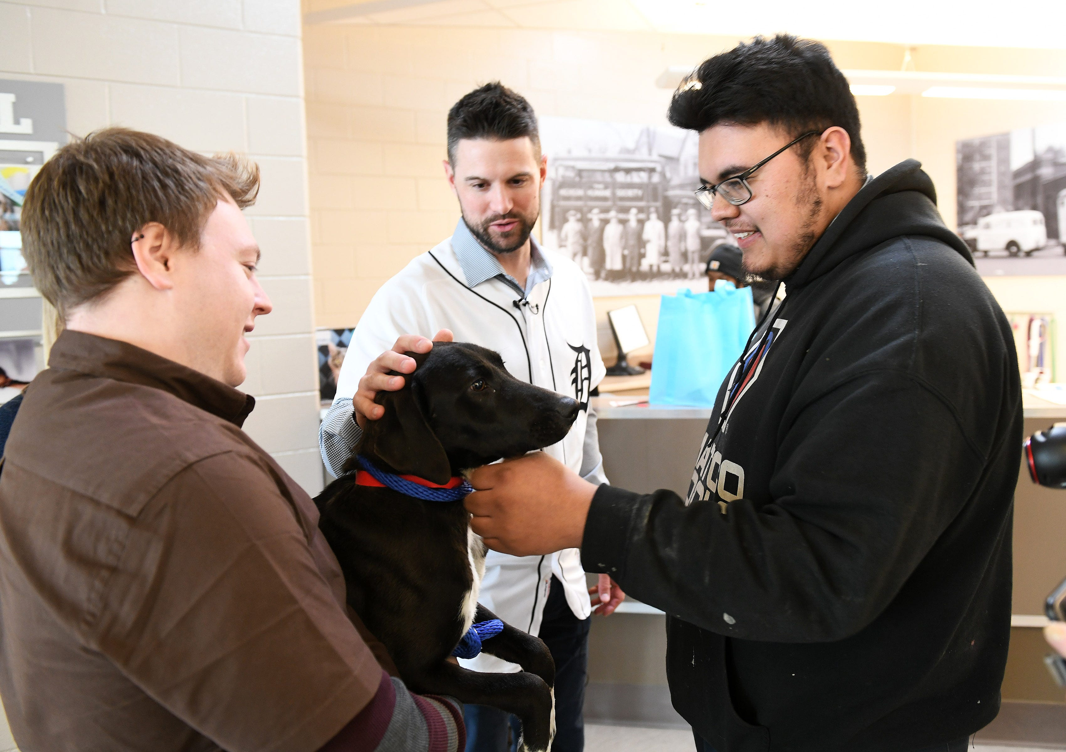While Michigan Humane Society animal transport driver Jeremy Colborn holds her, Tigers shortstop Jordy Mercer and Marcelo Alvarado, 24, of Detroit, right, pet Lark, a Labrador that Marcelo is adopting, at the Michigan Humane Society.