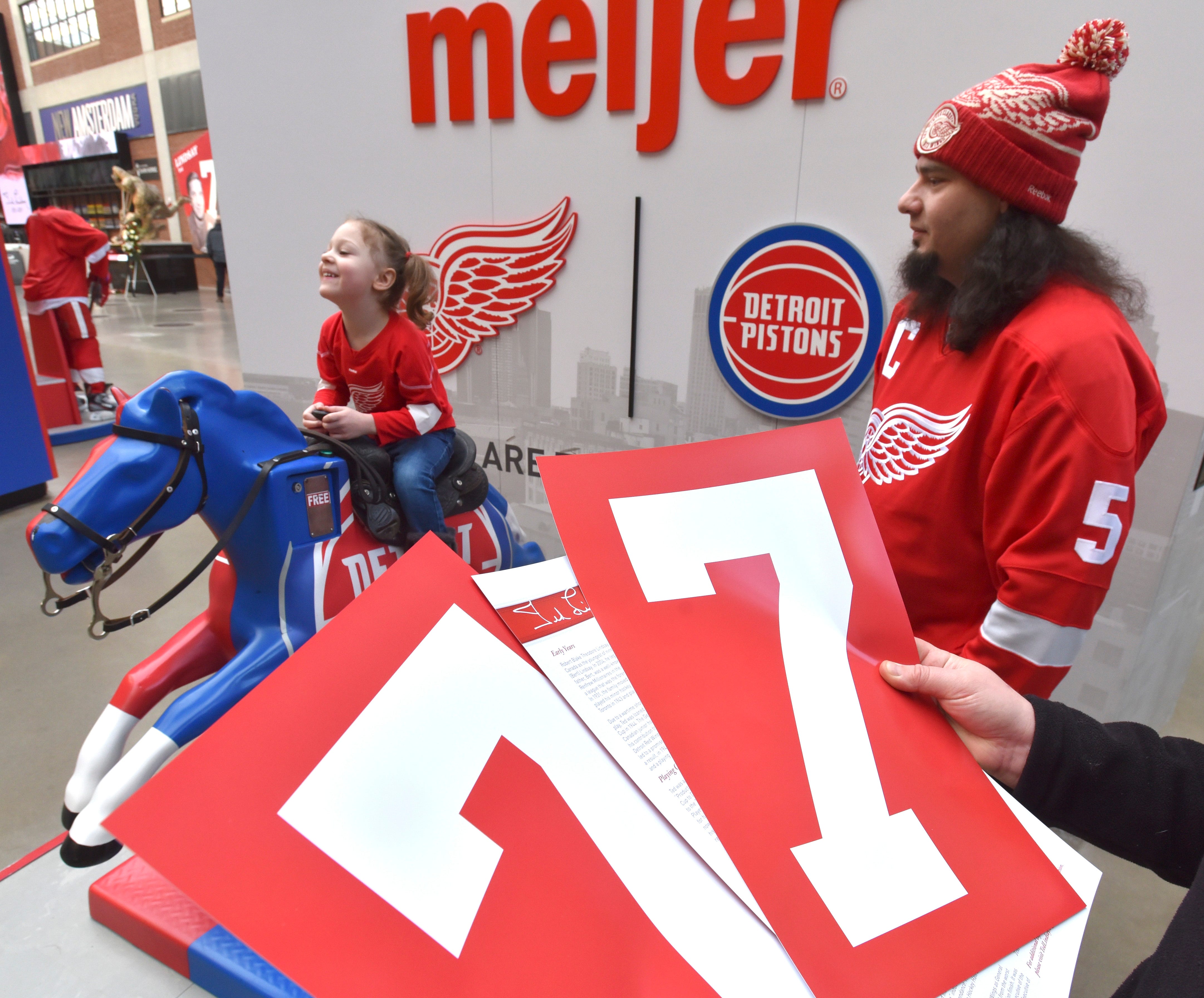 Nadea Lysyuk of Shelby Twp. shows off the #7 posters she and her family received after paying their respects to Ted Lindsay as her daughter, Kaylee Bommarito, 4, rides a mechanical horse near the Meijer entrance. Like many fans, husband Nick Bommarito wore his Red Wings gear.