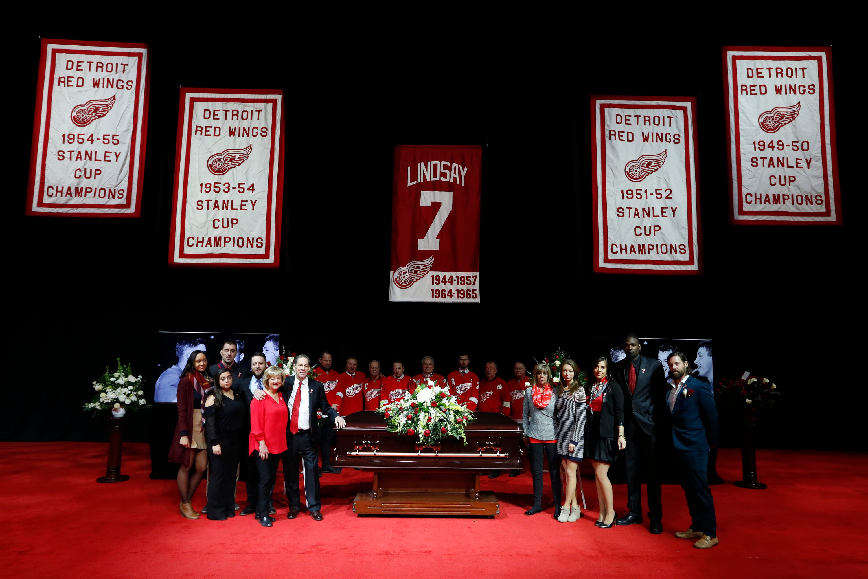 Family members pose with the casket of former Red Wing Ted Lindsay, with pallbearers behind it,  before the  public viewing. Lindsay's retired number hangs above.