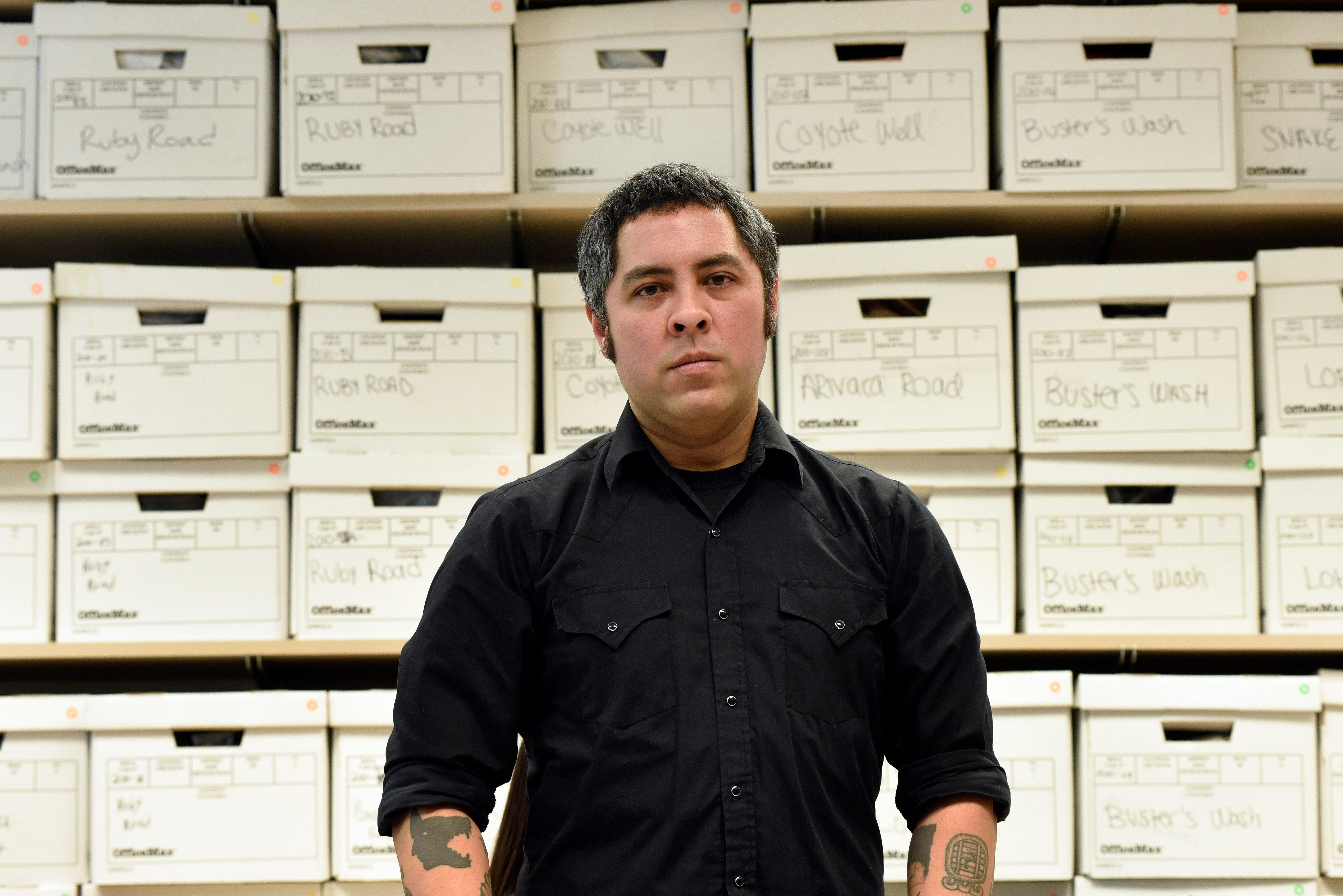 University of Michigan anthropologist Jason De León stands in his office with boxes of artifacts of things migrants left behind after crossing the Sonoran Desert.