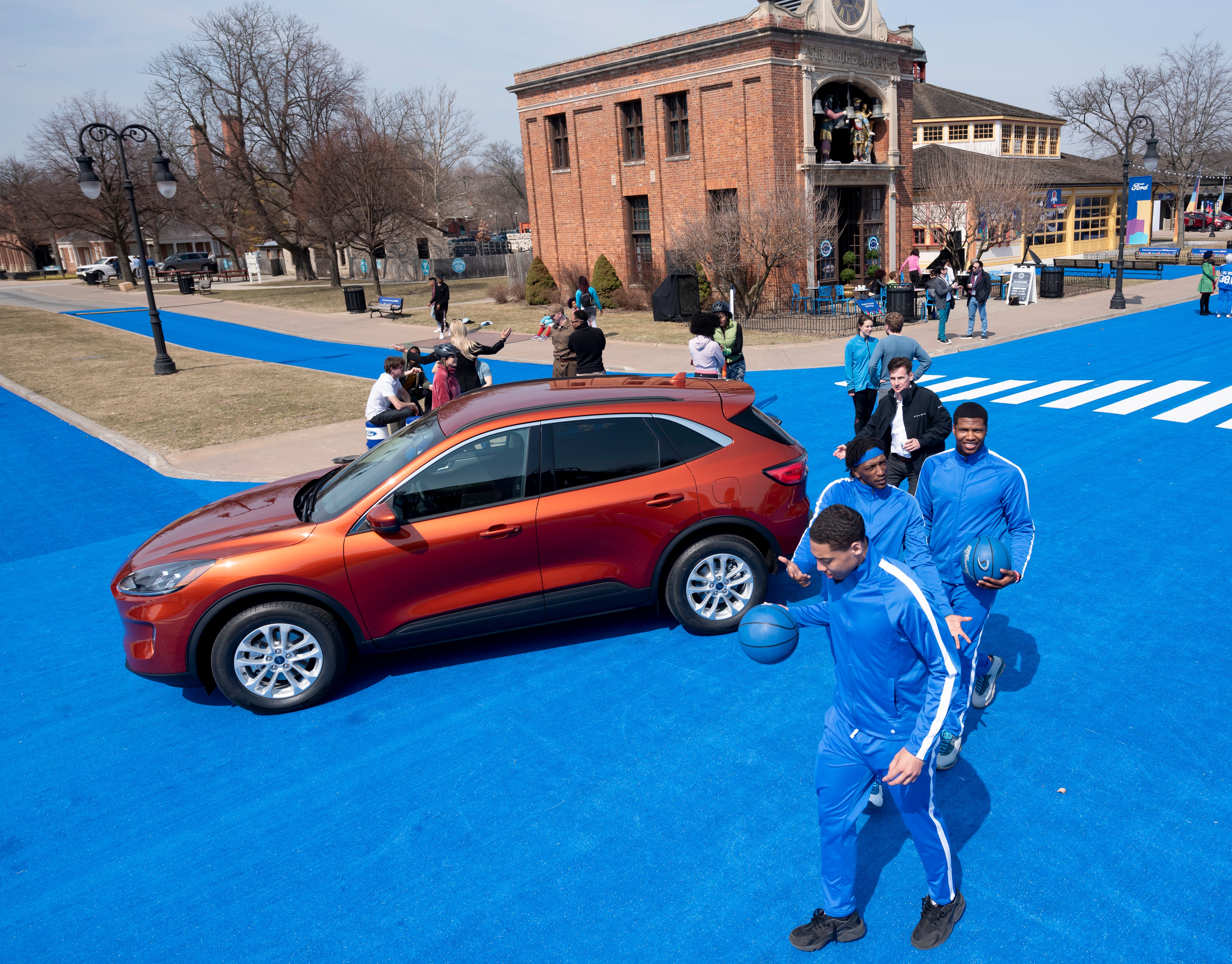 Members of the University of Michigan-Dearborn basketball team wander past a 2020 Ford Escape during a reveal at Greenfield Village, in Dearborn, March 28, 2019. Actors, artists and other performers participated in the event.
