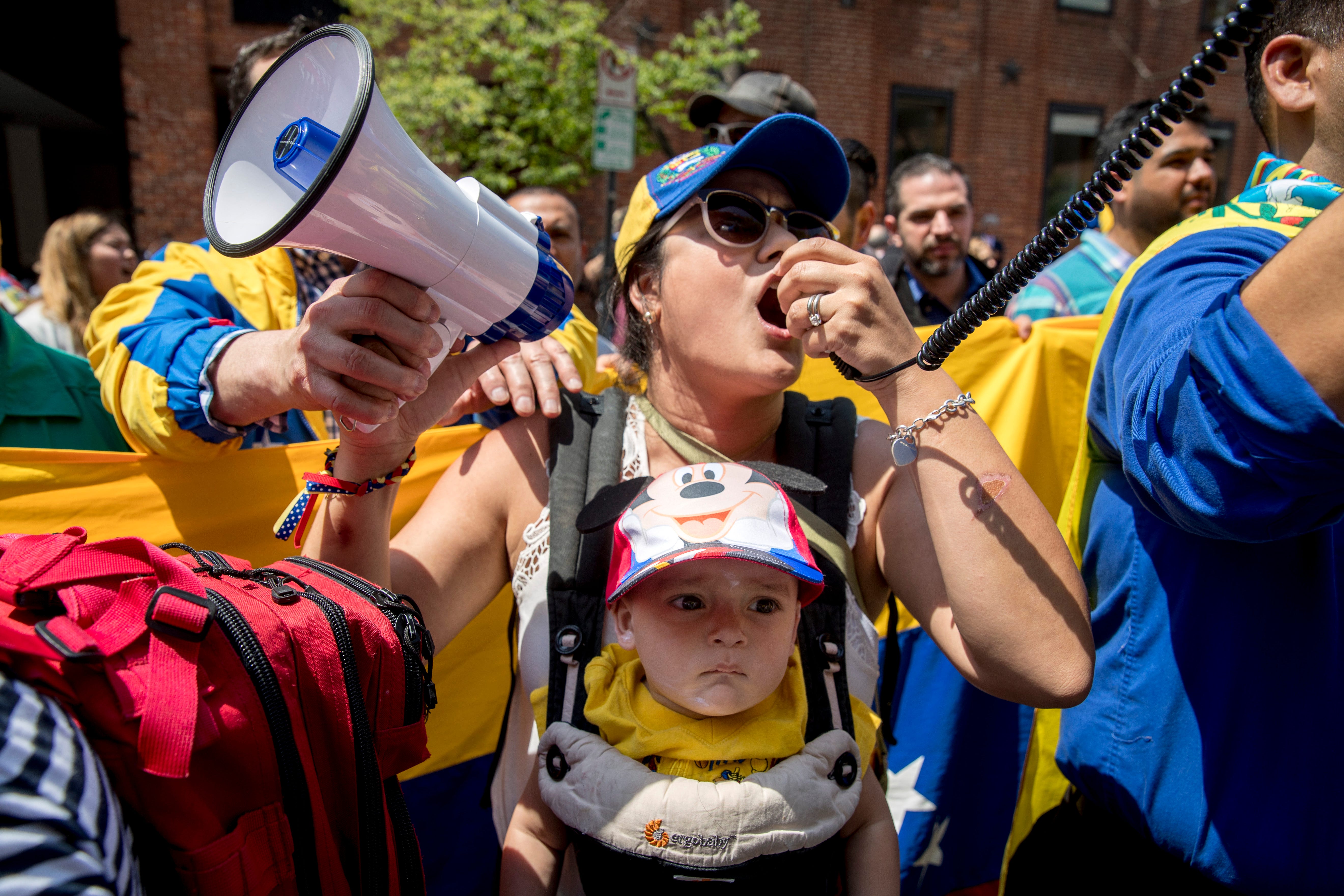 Carla Bustillos of Alexandria, Va., carries her son Carlos as she speaks on bullhorns with other supporters of pro interim government opposition leader Juan Guaido outside of the Venezuelan Embassy in Washington, April 30, 2019.