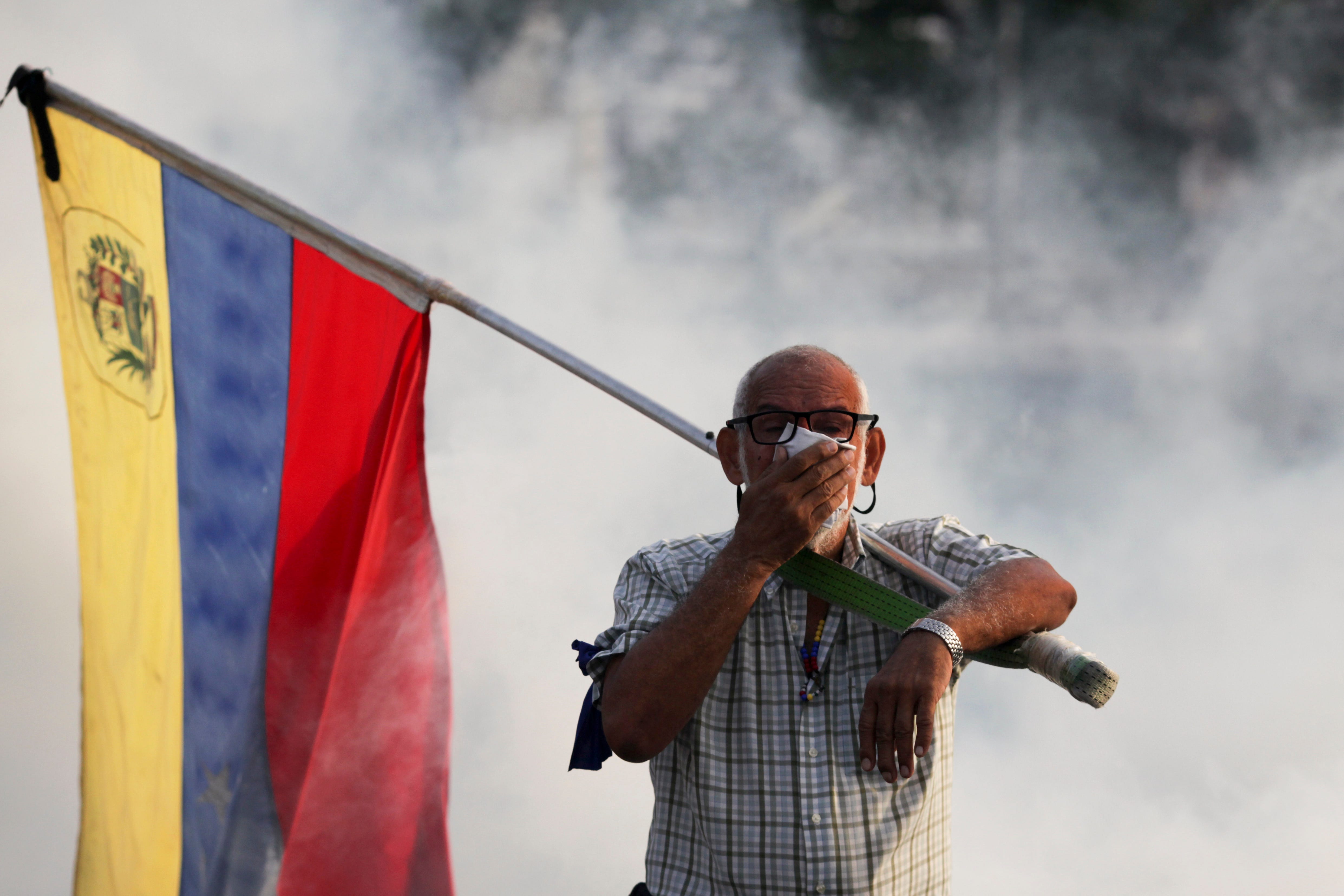 An opponent to Venezuelan President Nicolas Maduro carrying a Venezuelan flag covers his face amid tear gas fired by soldiers loyal to Maduro during an attempted military uprising to oust Maduro in Caracas, Venezuela, Tuesday, April 30, 2019. Venezuelan opposition leader Juan GuaidÃ³ and jailed opposition leader Leopoldo Lopez took to the streets with a small contingent of armed troops early Tuesday in a call for the military to rise up and oust Maduro.