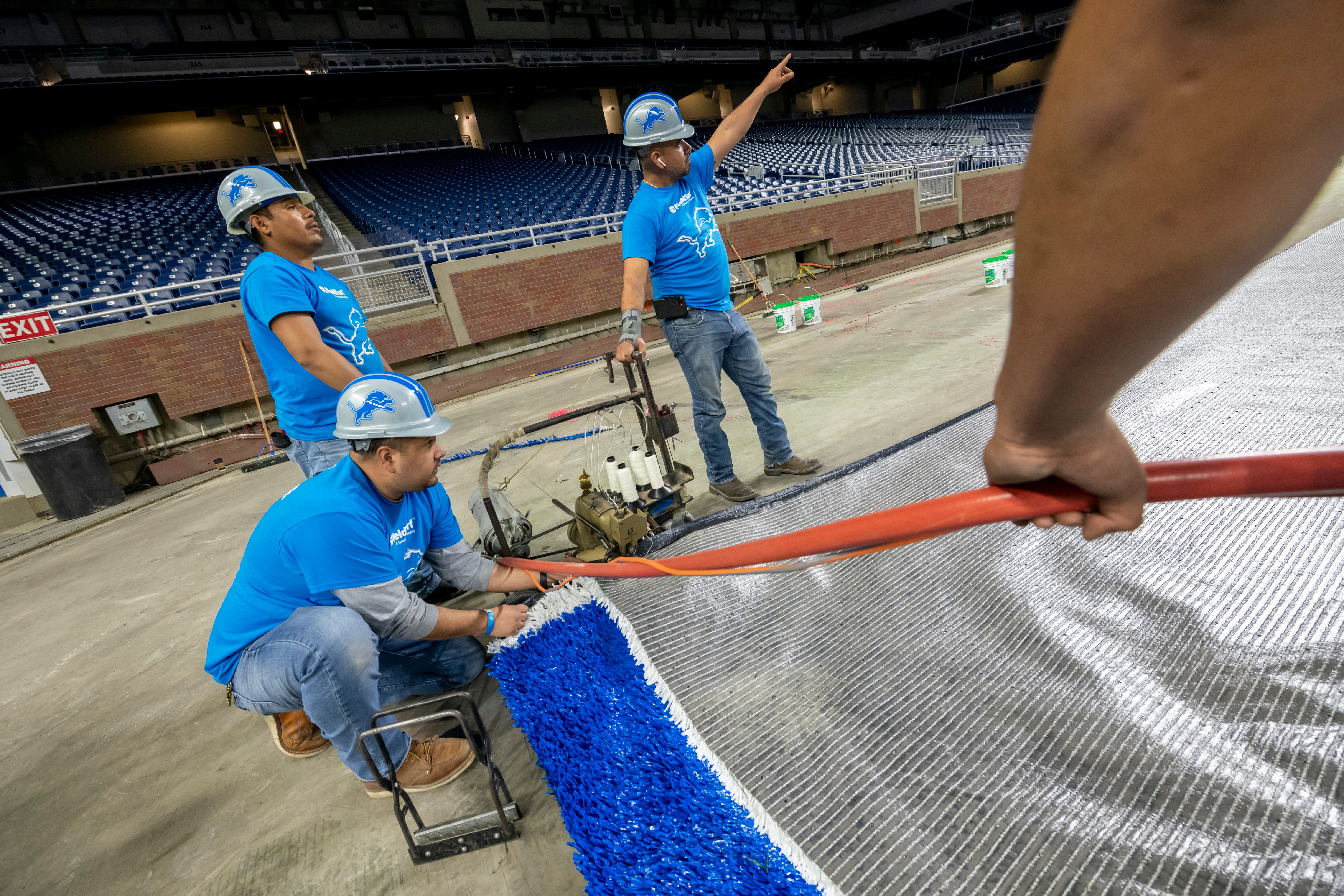 FieldTurf employees use an industrial sewing machine to connect two pieces of a new playing surface together at Ford Field.