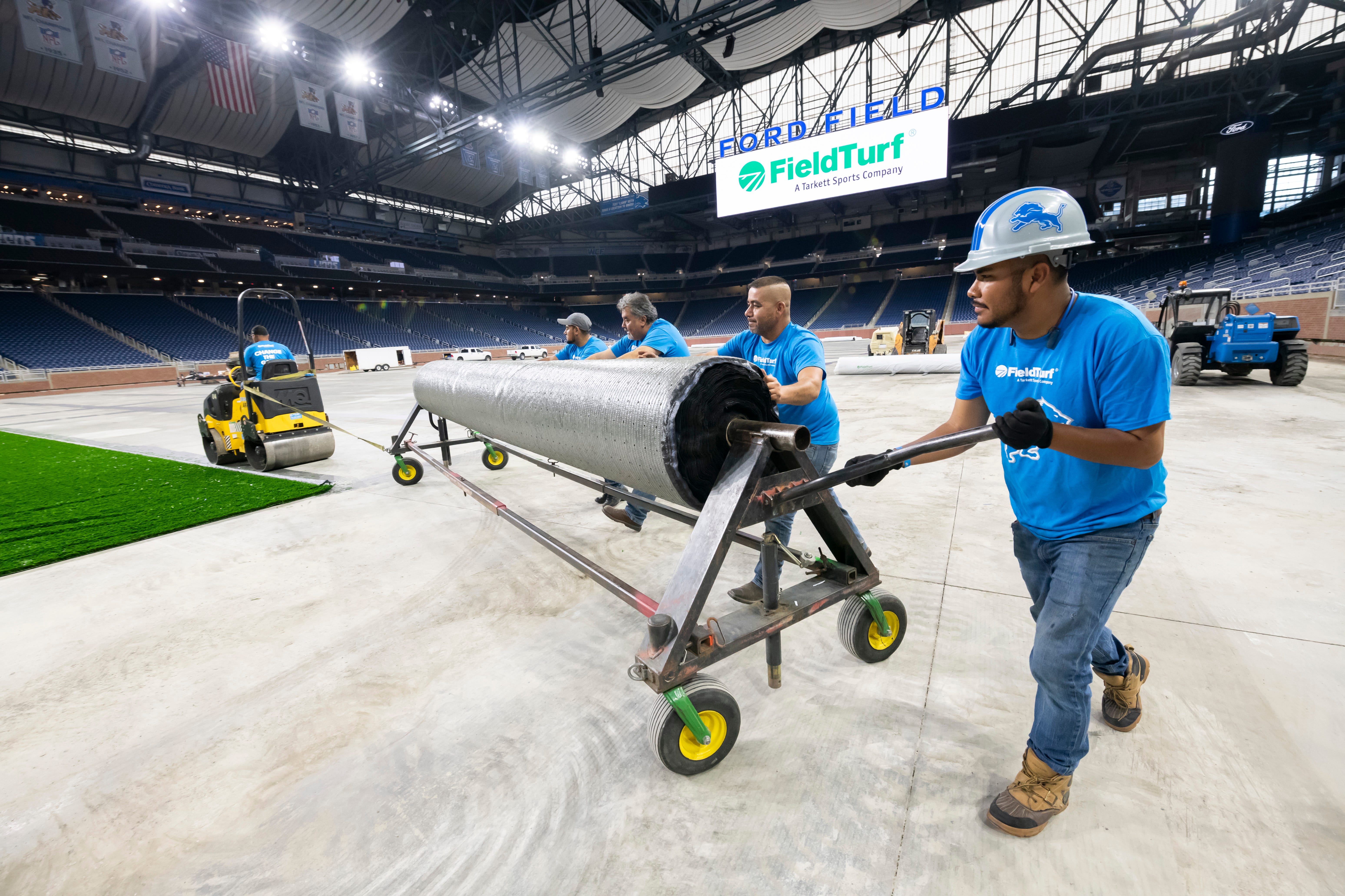 FieldTurf employees wheel out a roll of the playing surface while installing a new field at Ford Field.