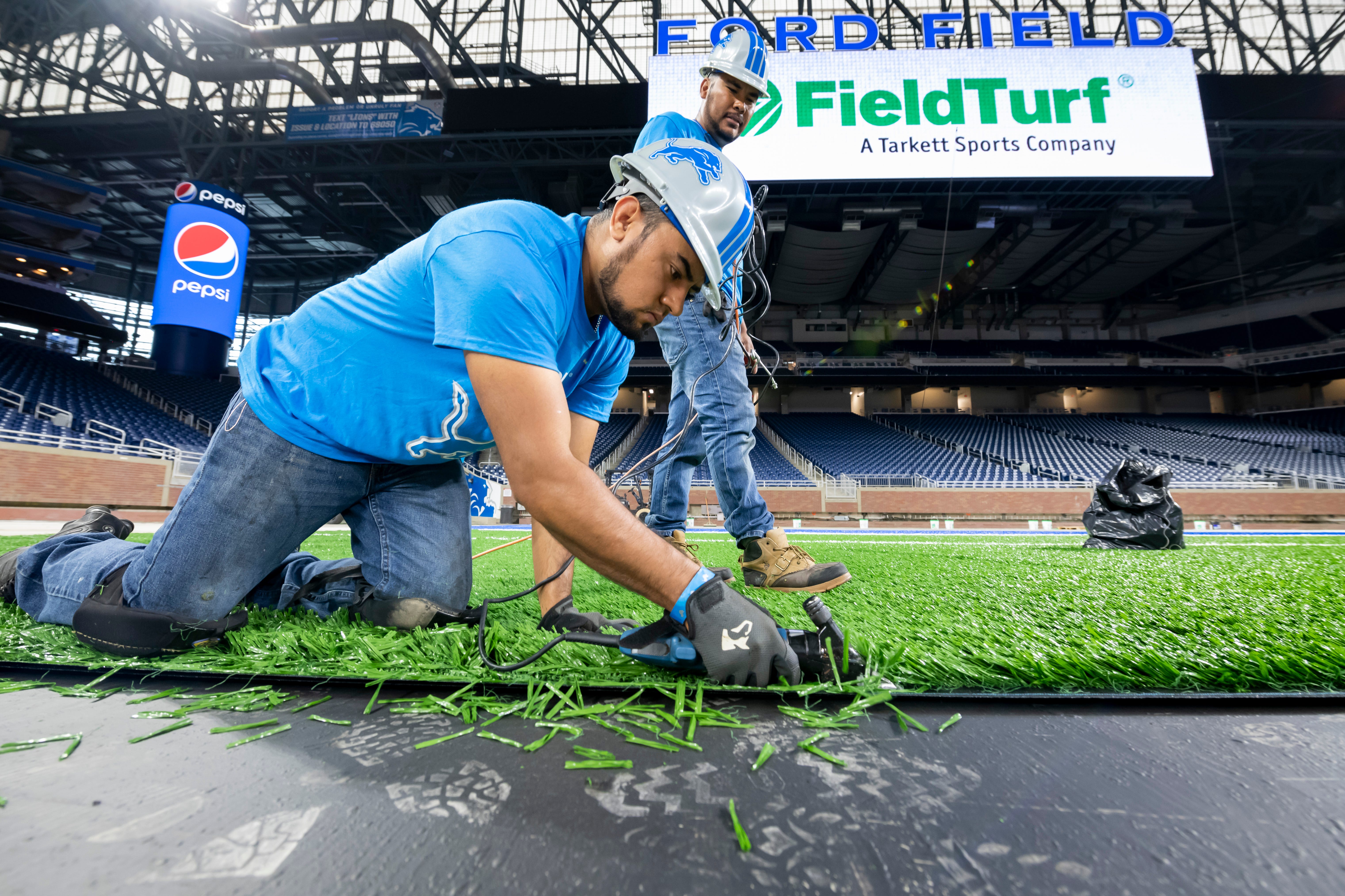 FieldTurf employee Jesus Casteneda uses sheep shearers to trim the edge of a piece of the playing surface during installation at Ford Field.