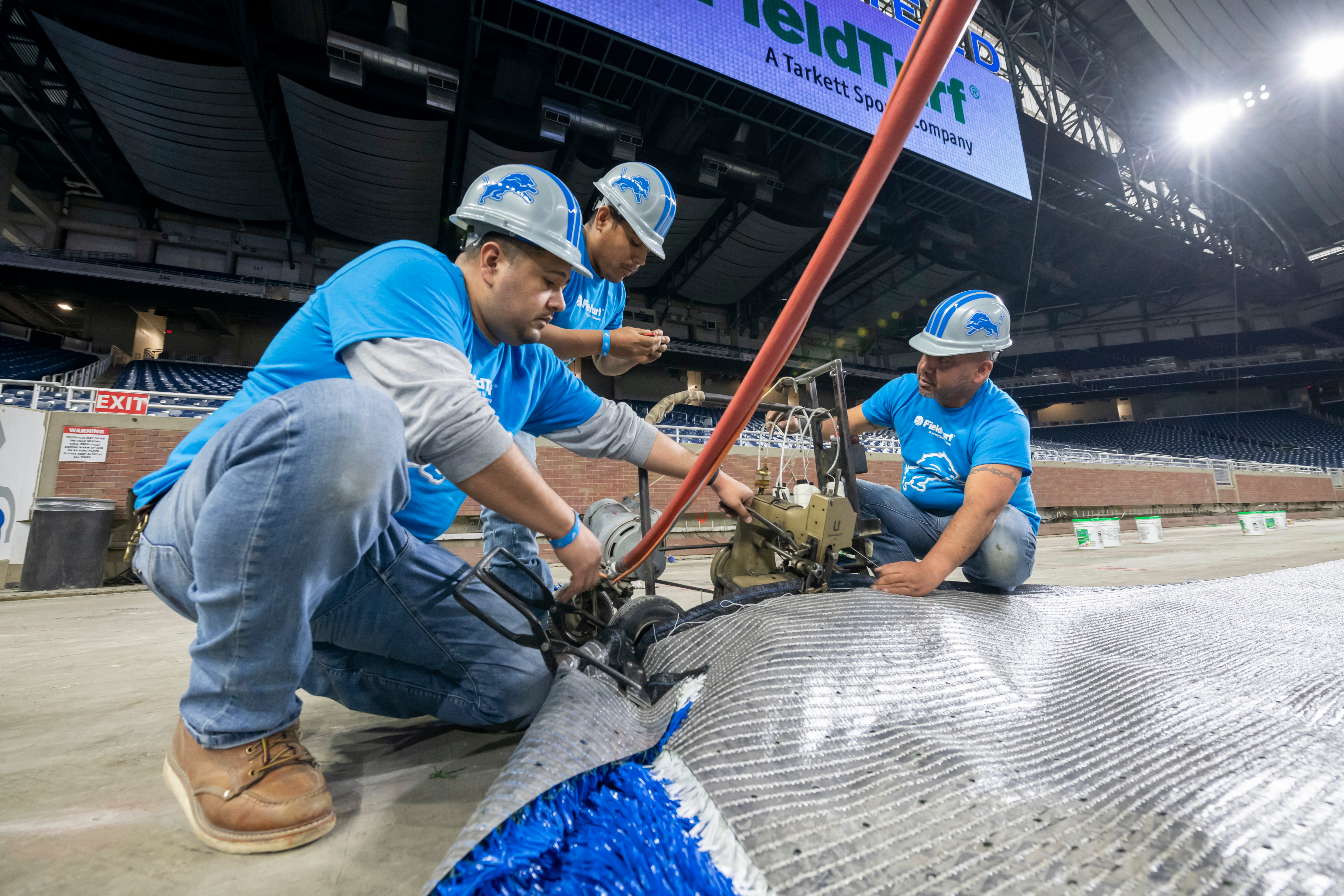 FieldTurf employees use an industrial sewing machine to connect two pieces of a new playing surface together.