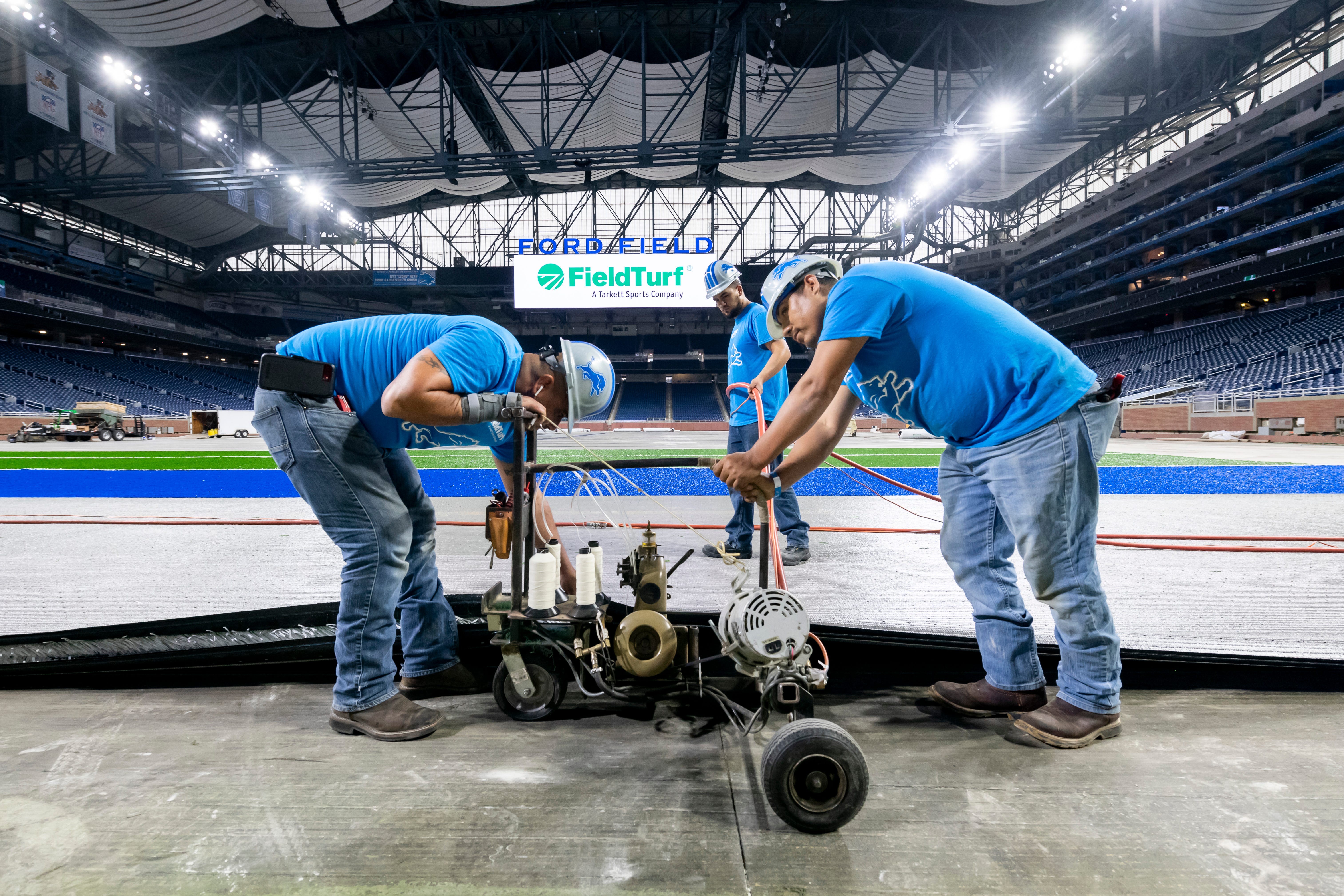 FieldTurf employees use an industrial sewing machine to connect two pieces of a new playing surface together at Ford Field.