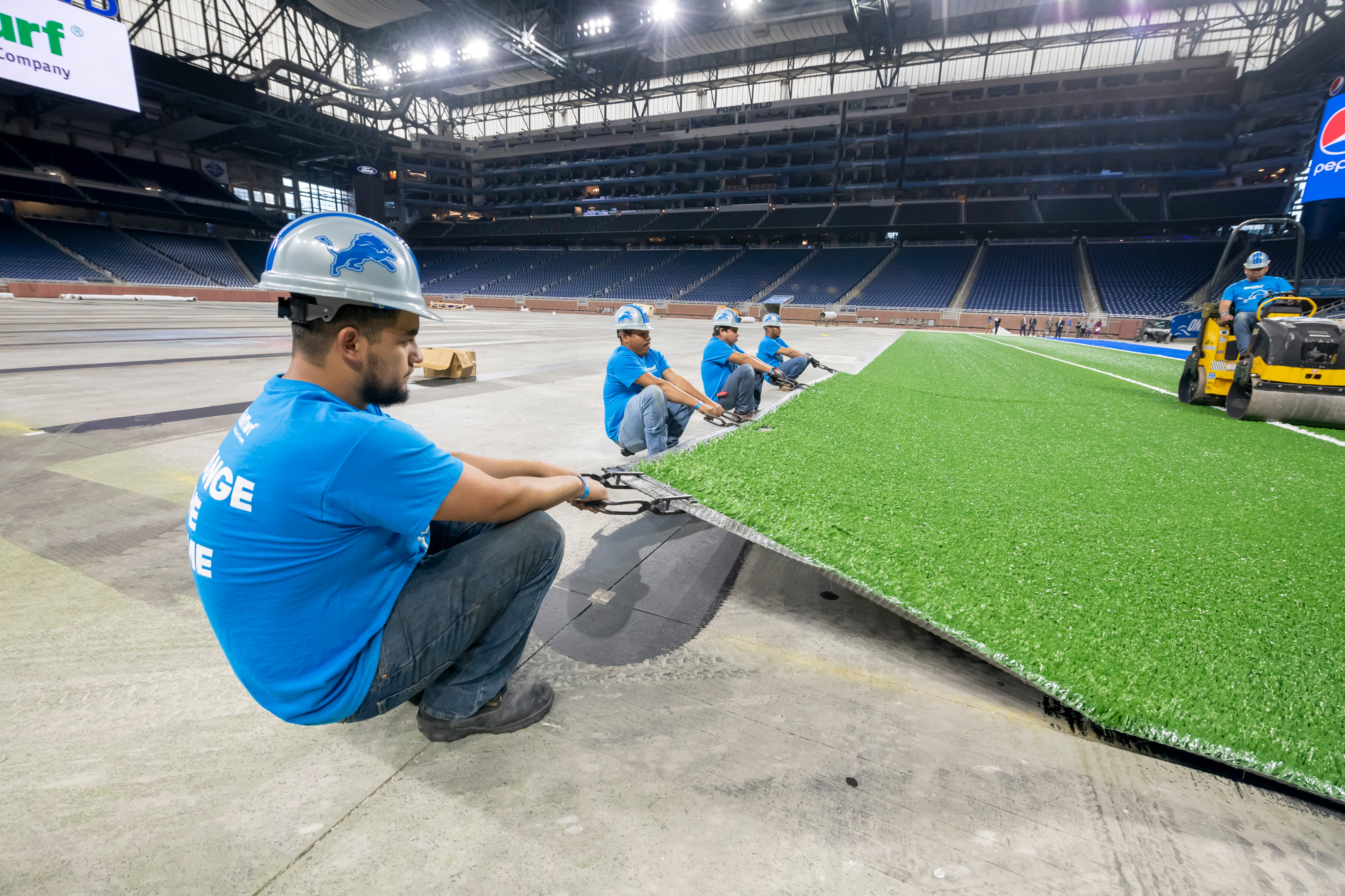 FieldTurf employees stretch the playing surface while installing it at Ford Field.