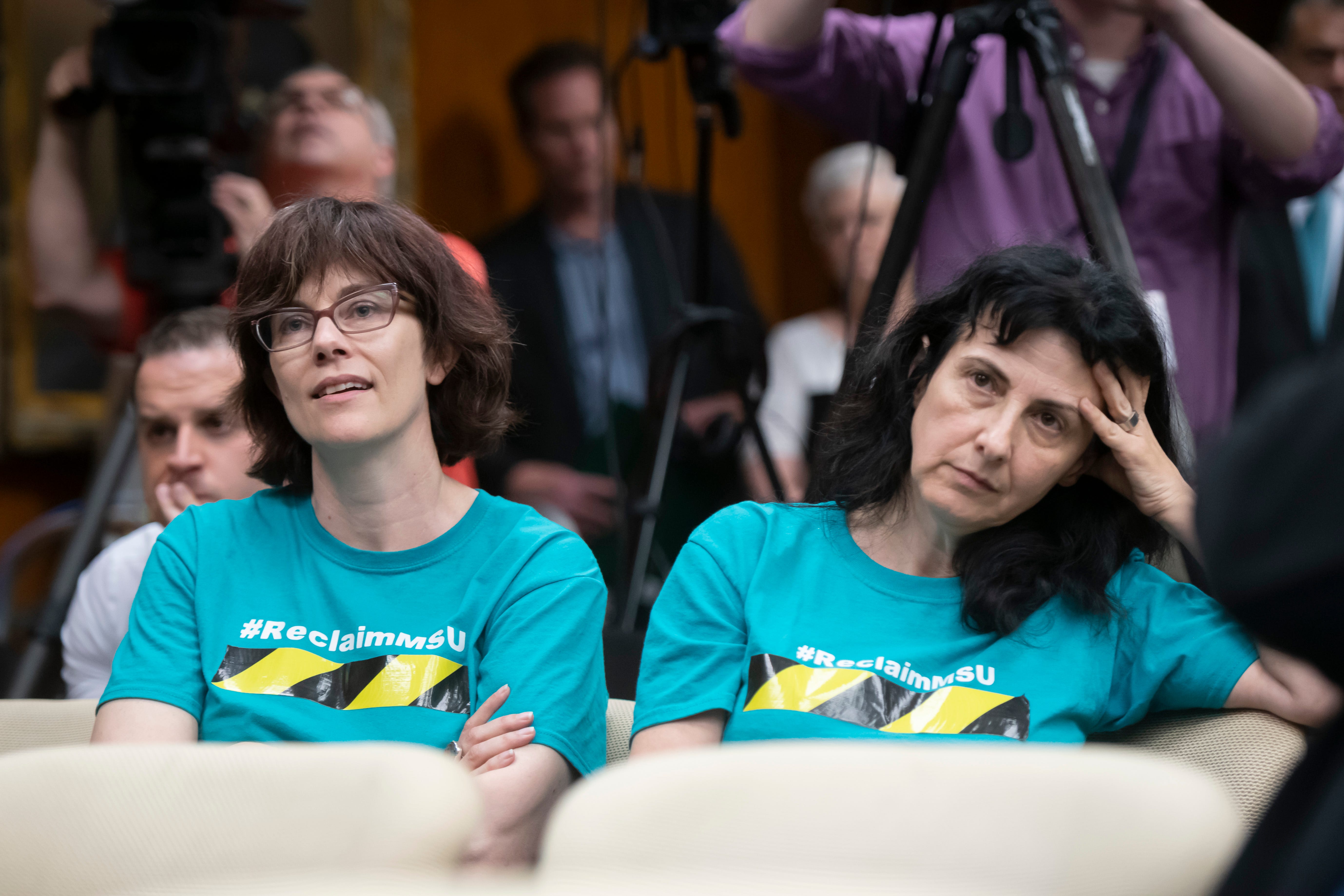 Michigan State professors Anna Pegler-Gordon, left, and Andaluna Borcila listen during a special session of the Michigan State University board of trustees that voted to elect Samuel Stanley Jr. as the 21st president of the university, May 28, 2019.  The pair are members of Reclaim MSU, an organization of staff, students and alumni that demand "a culture of transparency and accountability" at the university.