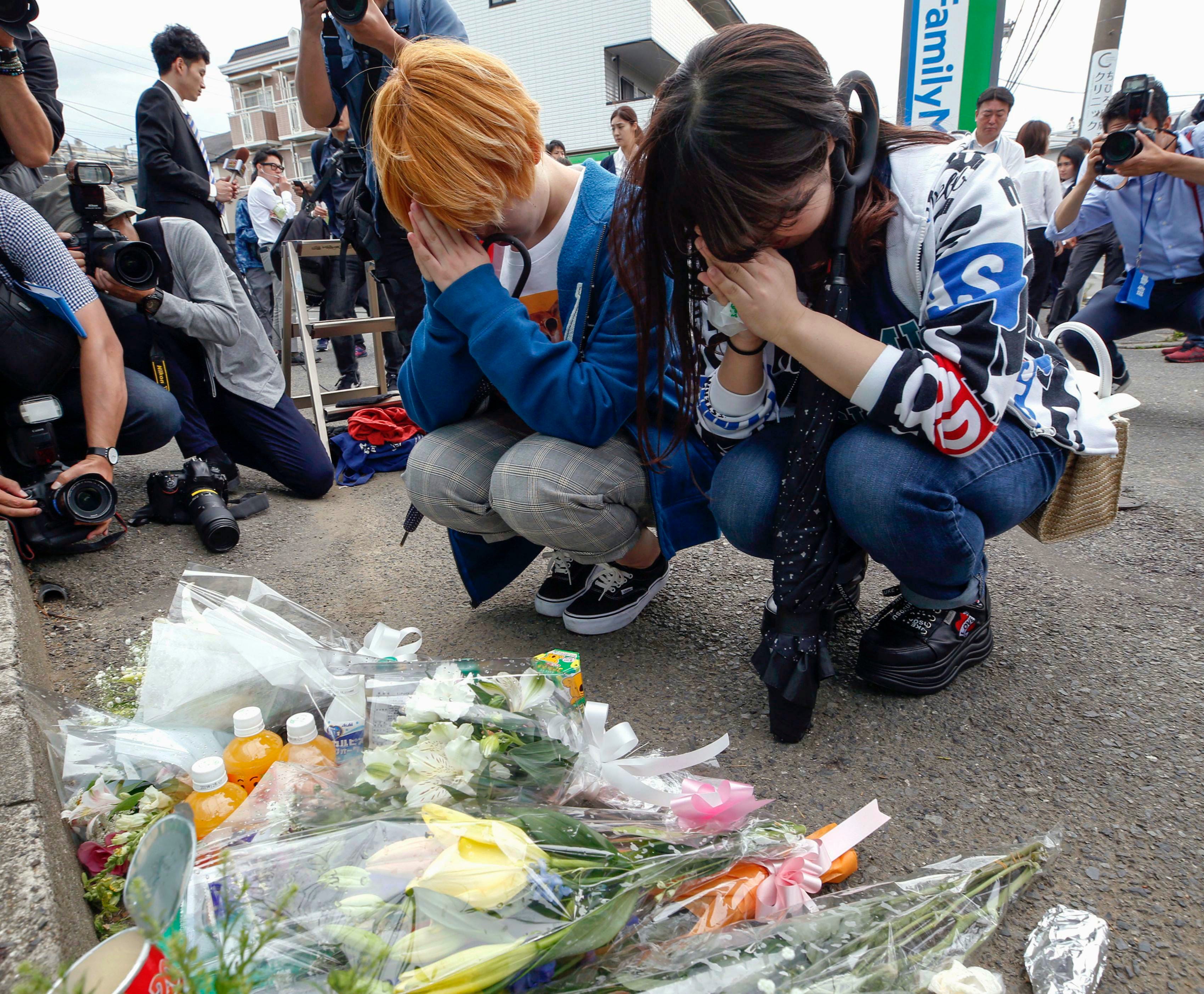 Women pray after offering flowers near the scene where a man wielding a knife attacked commuters in Kawasaki, near Tokyo Tuesday, May 28, 2019.
