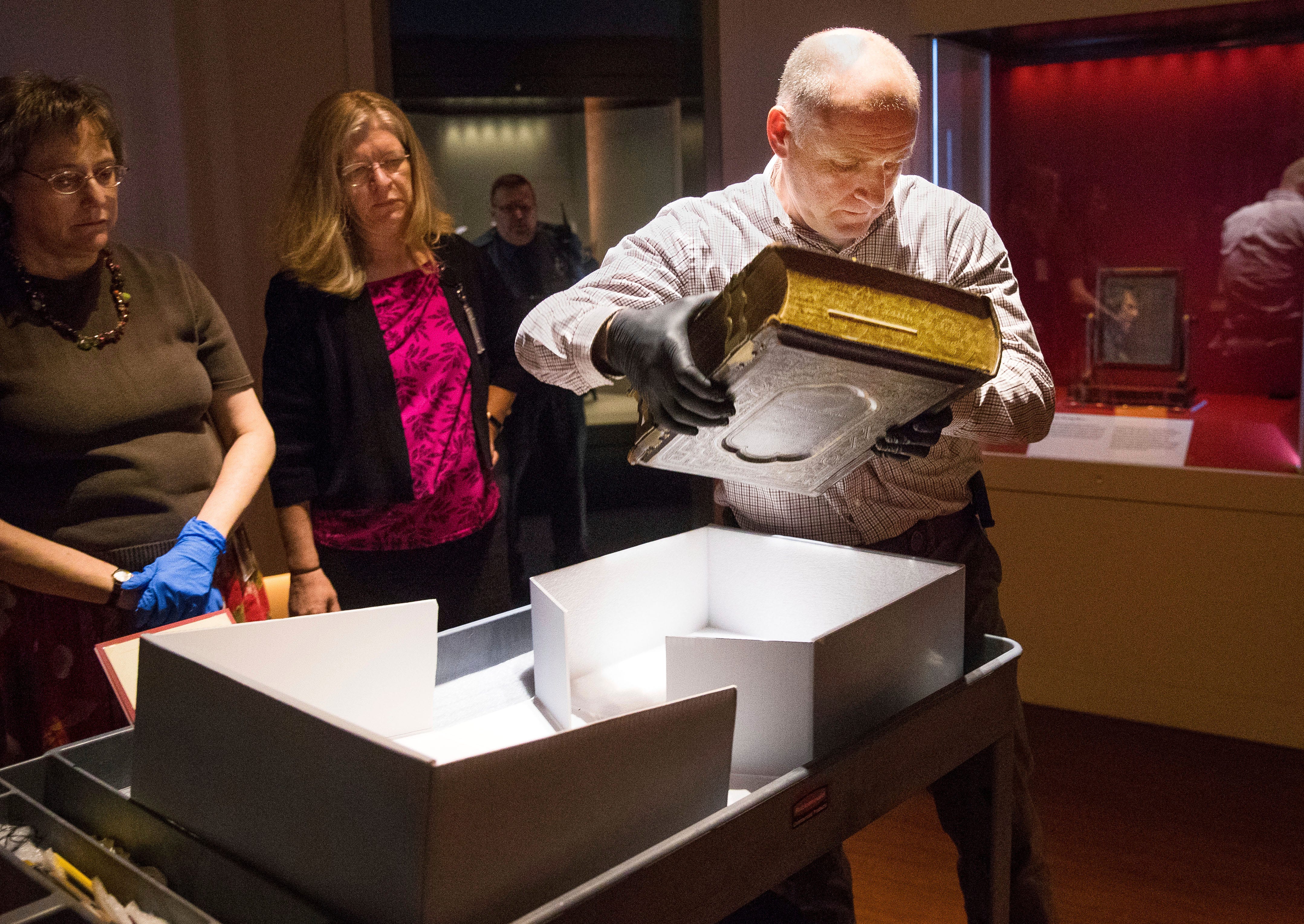 Mike Casey, Exhibits Project Manager at the Abraham Lincoln Presidential Museum, moves the newly acquired Bible into an exhibit at the museum. Abraham Lincoln Presidential Library and Museum Conservator Bonnie Parr and Carla Smith, registrar for the Abraham Lincoln Presidential Library and Museum, are at left.