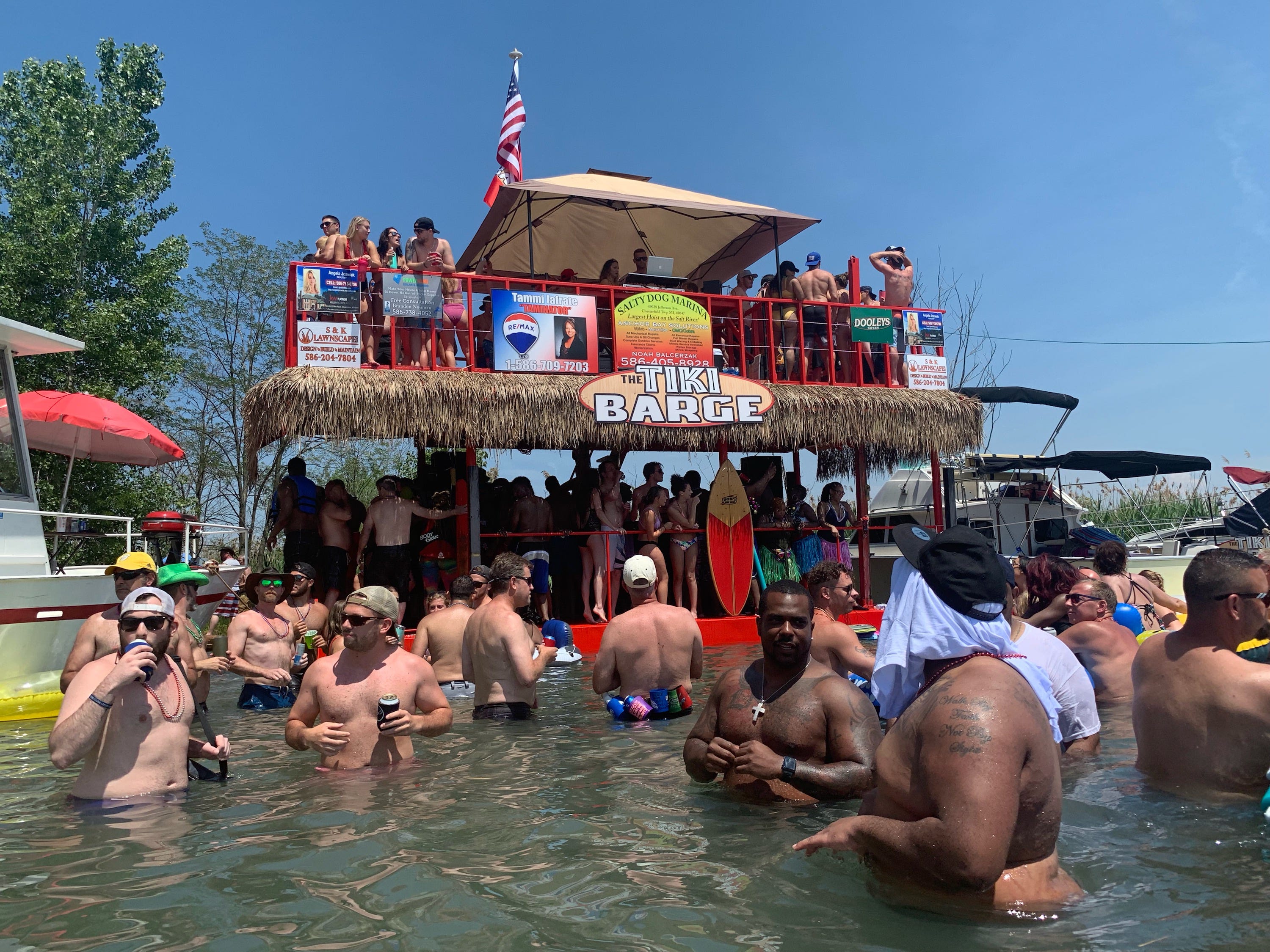 Jobbie Nooner revelers congregate in waist-high waters surrounding the Tiki Barge party boat on what was a beach area in previous years... eliminated this year by high lake water levels on Lake St. Clair at Gull Island Friday, June 28, 2019.