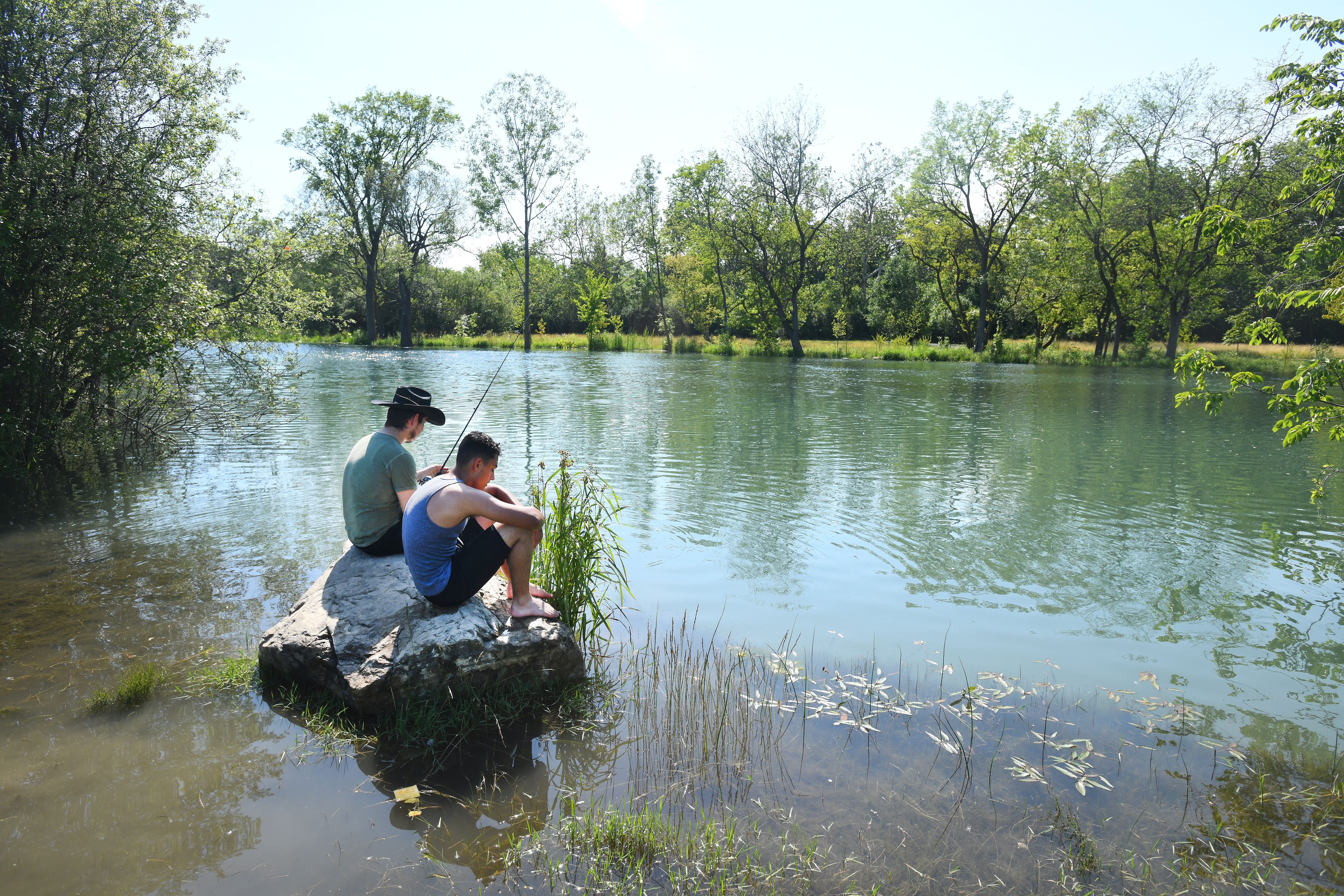 Michael Truesdell and Nathaniel Cecil of Lincoln Park fish from a rock surrounded by water near the usual bank of the Trenton Channel in Elizabeth Park in Trenton, Michigan on July 1, 2019.