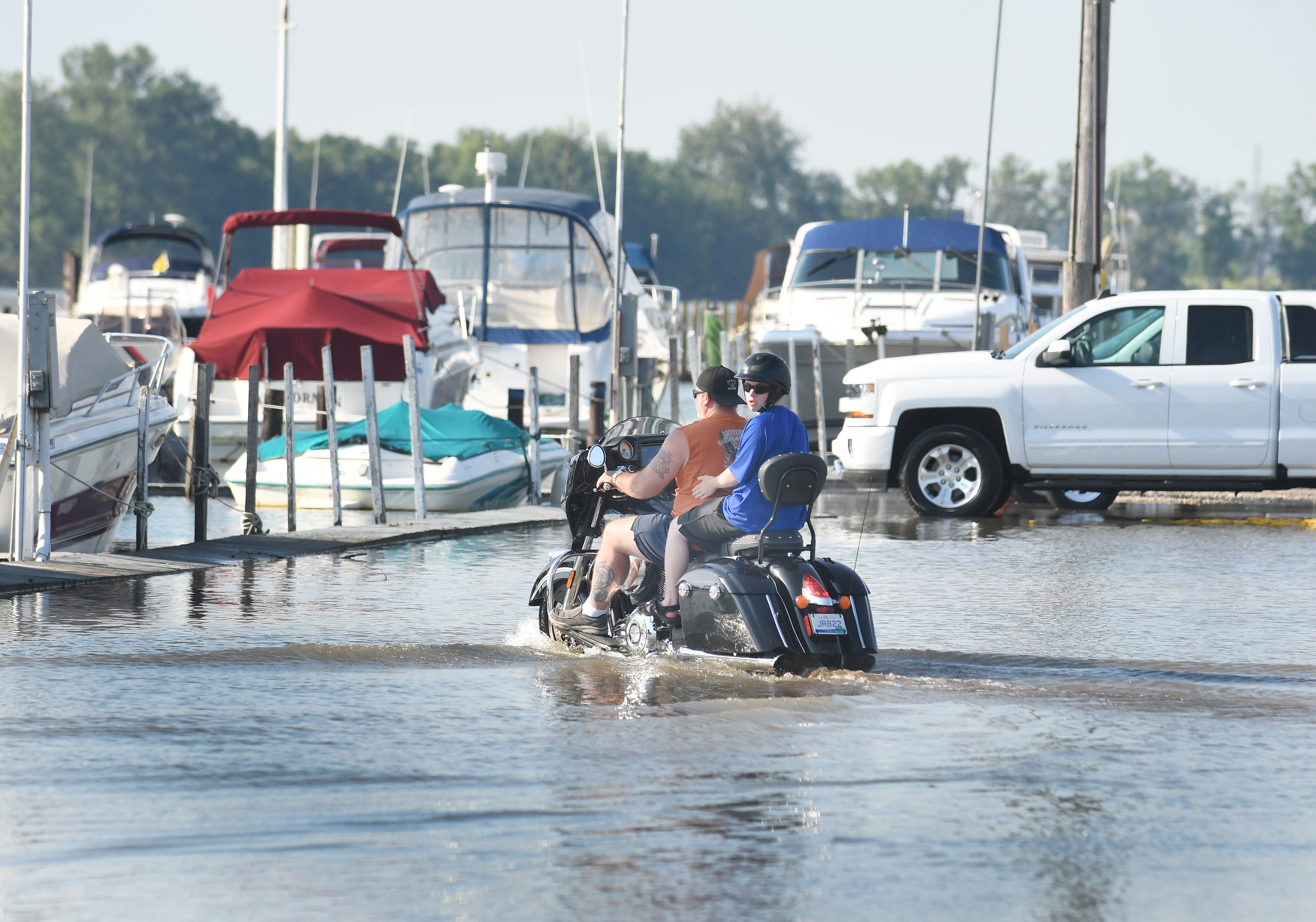 A motorcycles and passenger traverse high water on a usually dry parking lot at the Humbug Marina in Gibralter, Michigan on July 1, 2019.