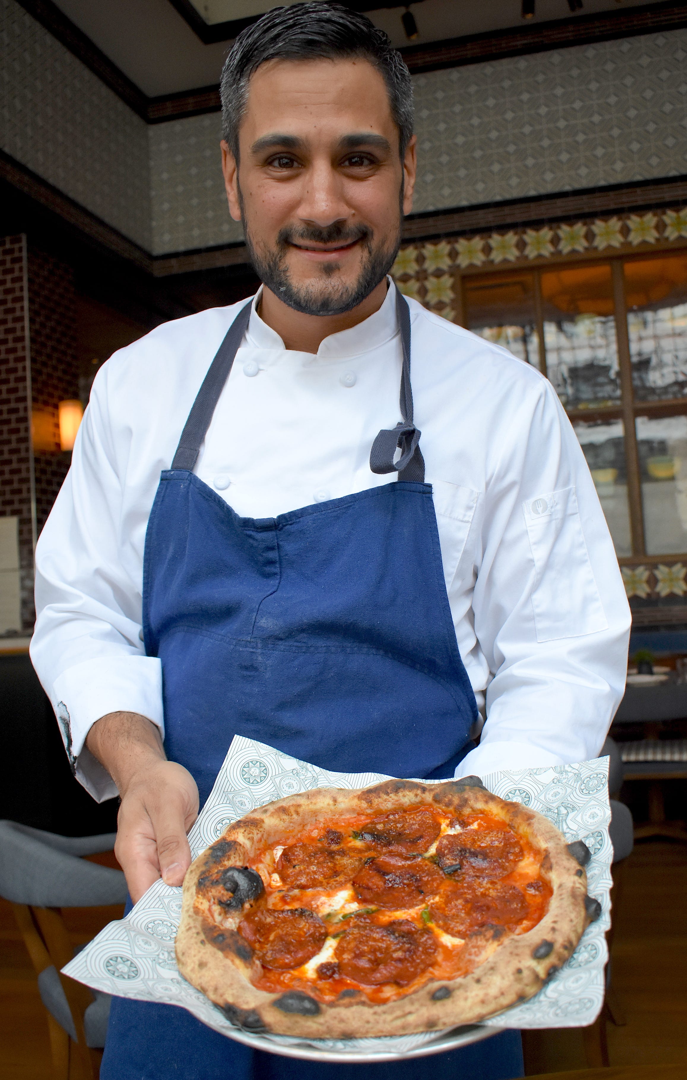 Chef de cuisine Cory Barberio shows off an " OG " pie, hot out of the wood-fired oven. The pizza is topped with pepperoni, ' nduja, and Fresno chilies.