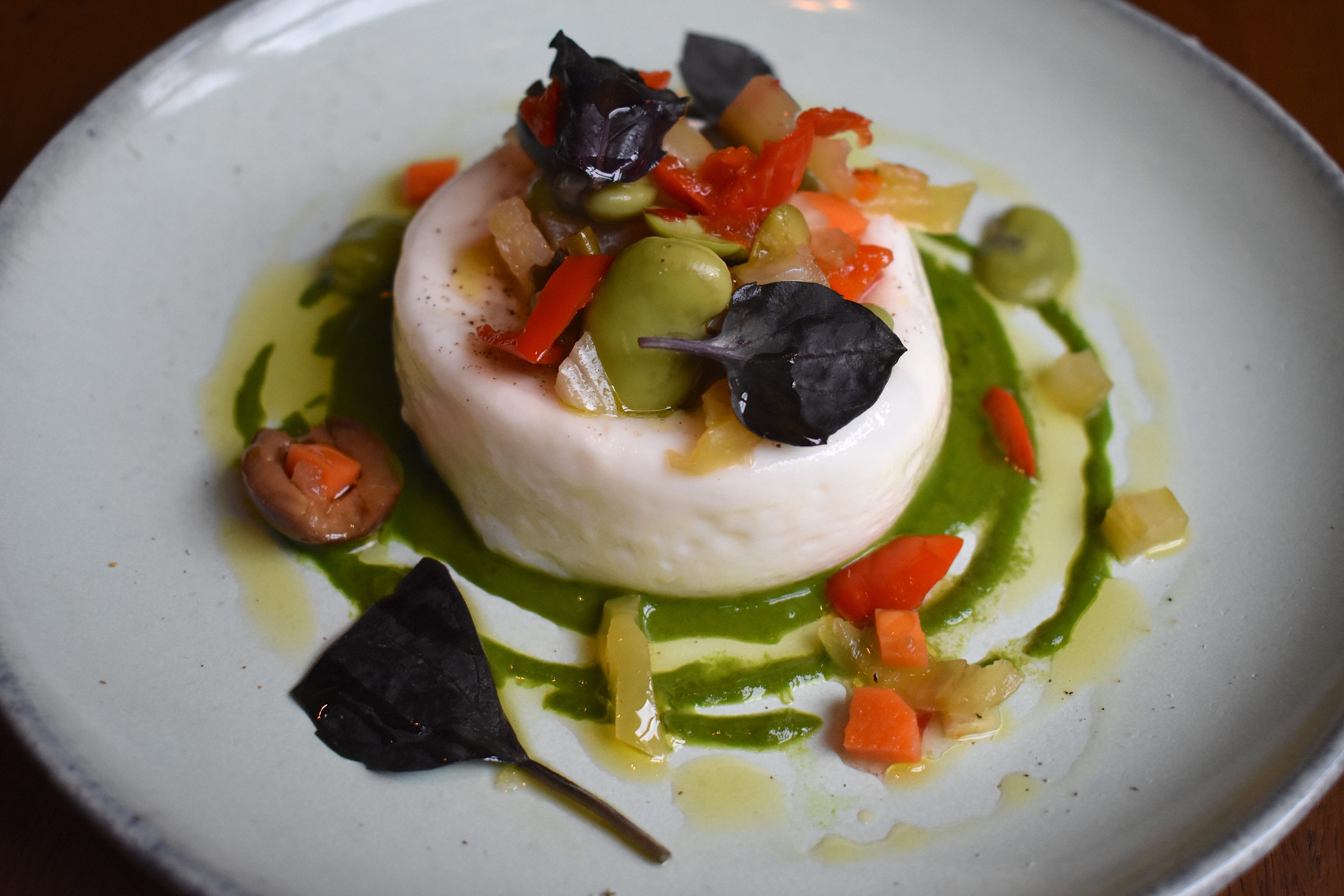 A creamy burrata appetizer is garnished with fava beans, arugula pesto, and opal basil.