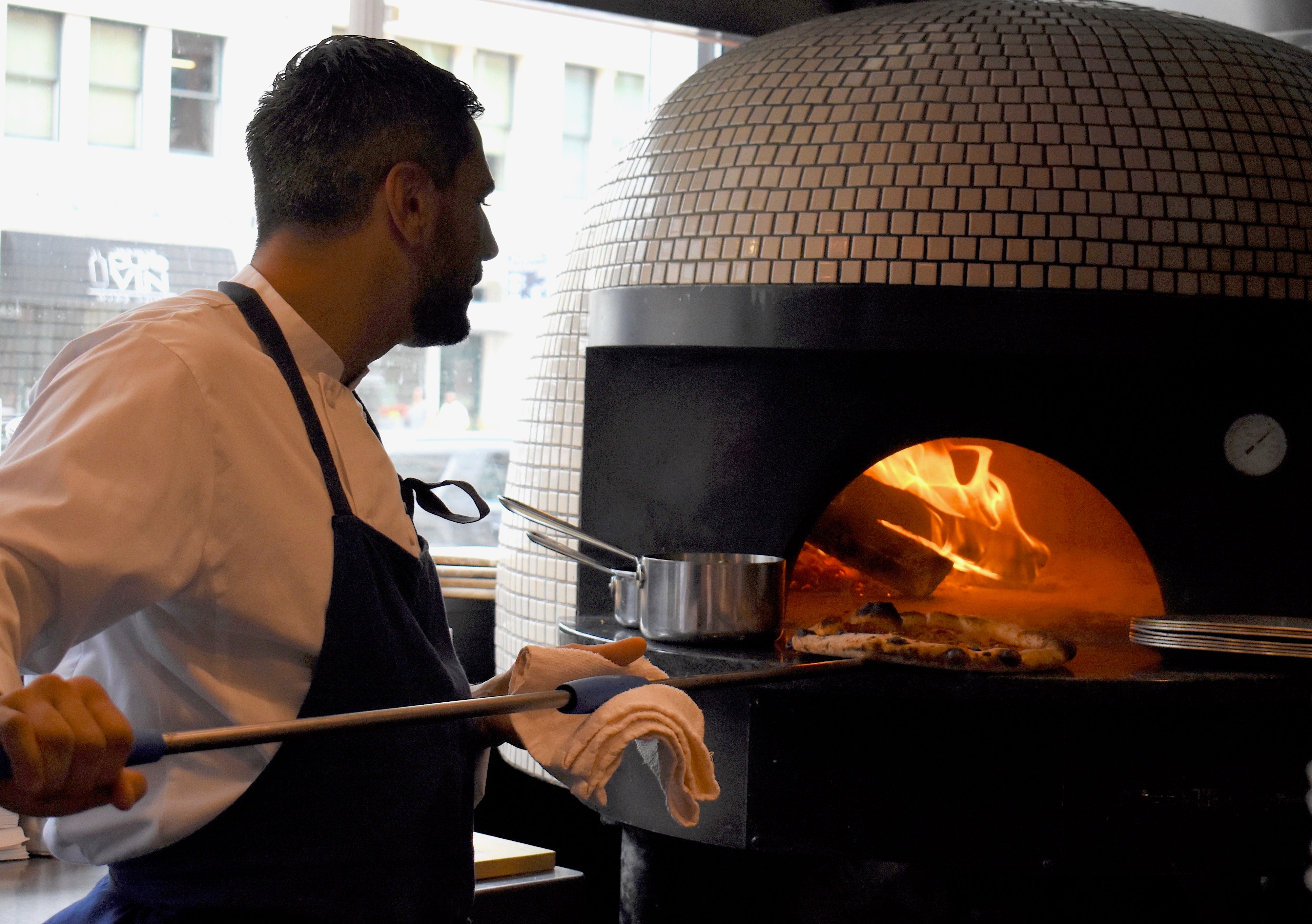 Chef de cuisine Cory Barberio eases an " OG " pie out of the wood-fired oven. The pizza is topped with pepperoni, ' nduja, and Fresno chilies.