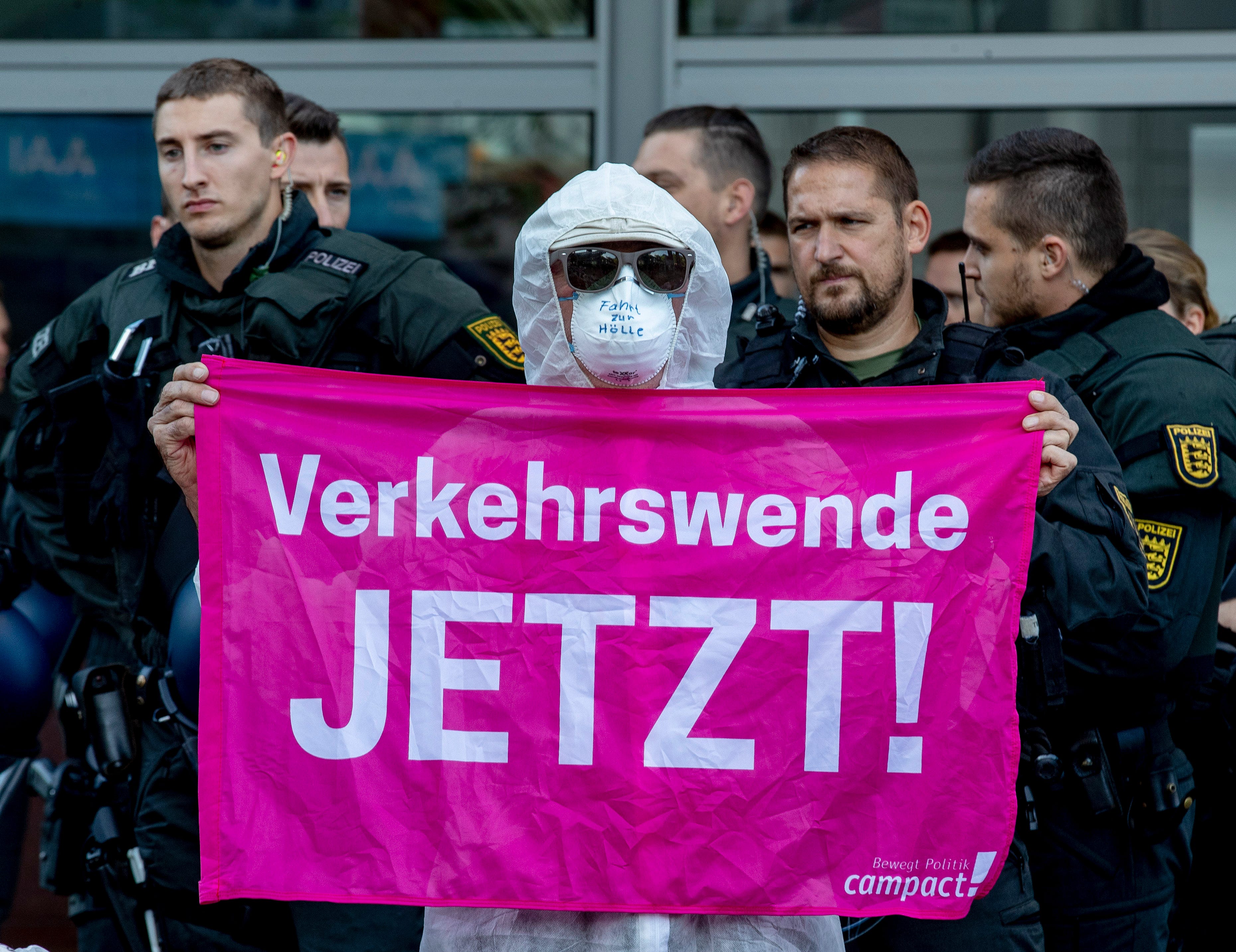 An activist holds a banner reading "traffic change now" as he blocks the main entrance of the fairground in Frankfurt, Germany, Sunday, Sept. 15, 2019.