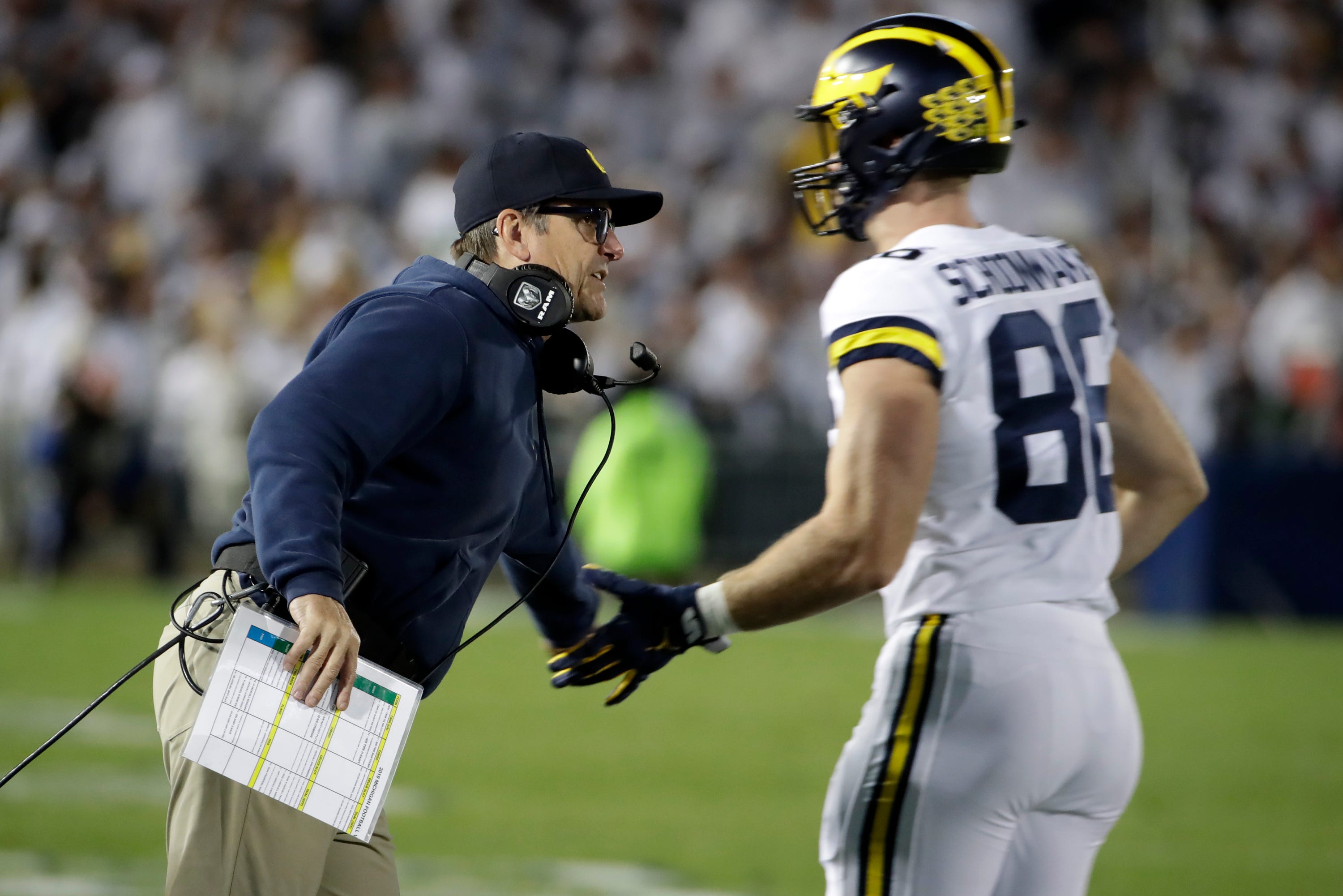 Michigan head coach Jim Harbaugh, left, greets tight end Luke Schoonmaker (86) as he returns to the sidelines during the first half.
