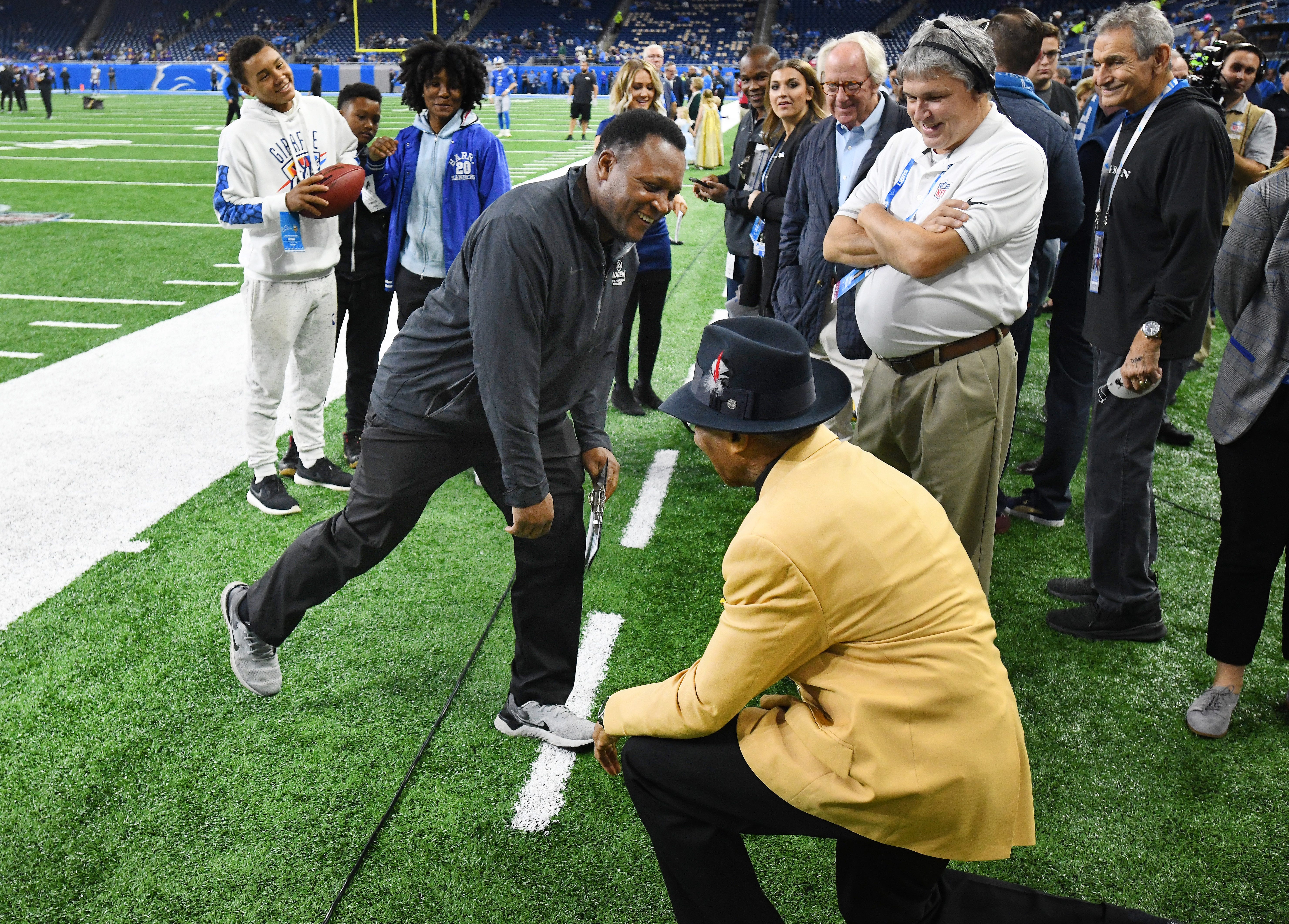 NFL Hall of Fame defensive back Lem Barney takes a knee to NFL Hall of Fame running back Barry Sanders as the two goof around on the sidelines before the Lions take on the Vikings at Ford Field.