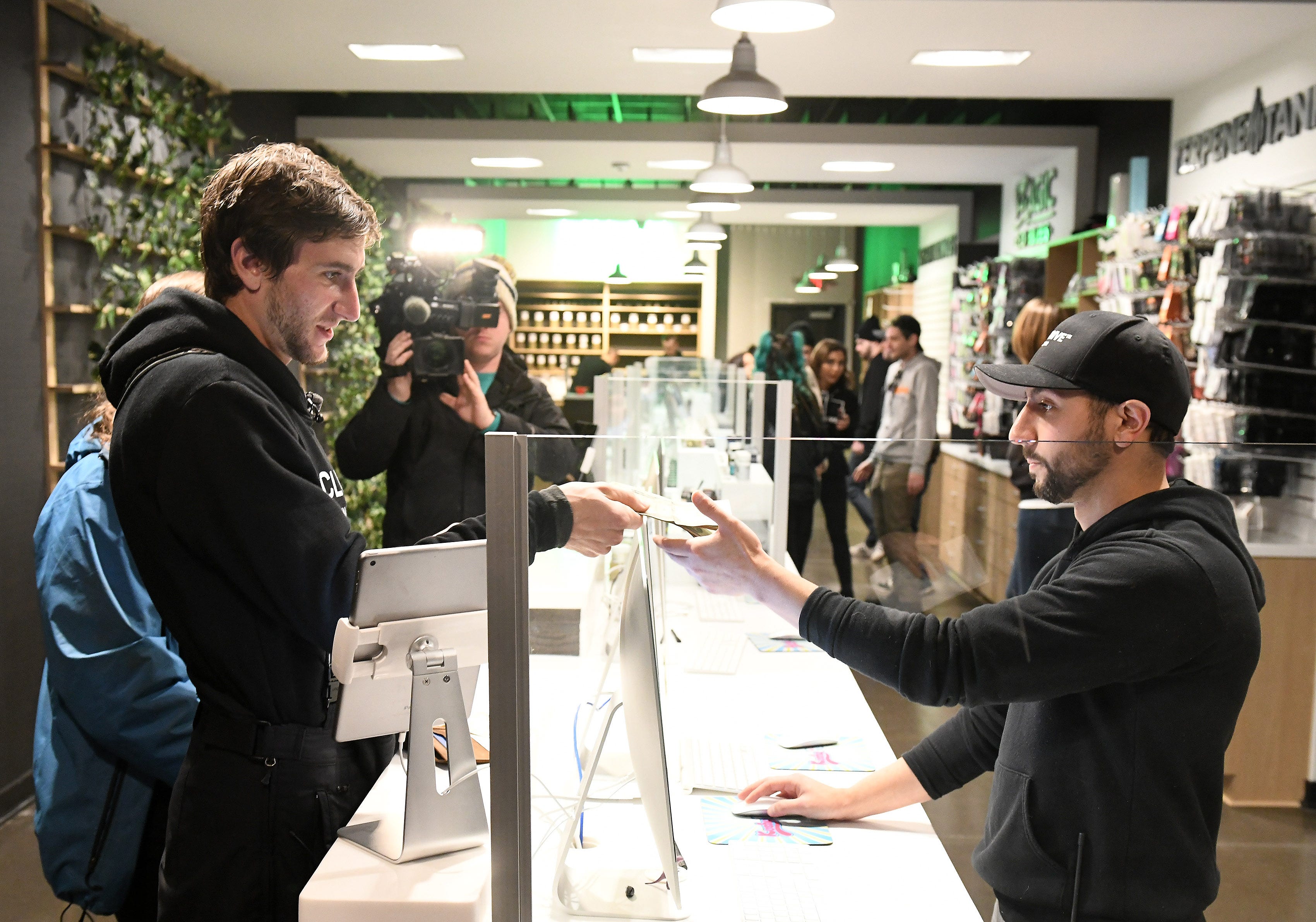 Kelly Savage, 25, of Ohio, left, makes the first purchase of recreational marijuana giving cash to general manager Nick Warra, right, at Exclusive Provisioning Center in Ann Arbor, Mich. on Dec. 1, 2019.  Savage has Type 1 diabetes and also uses marijuana socially.
(Robin Buckson / The Detroit News)