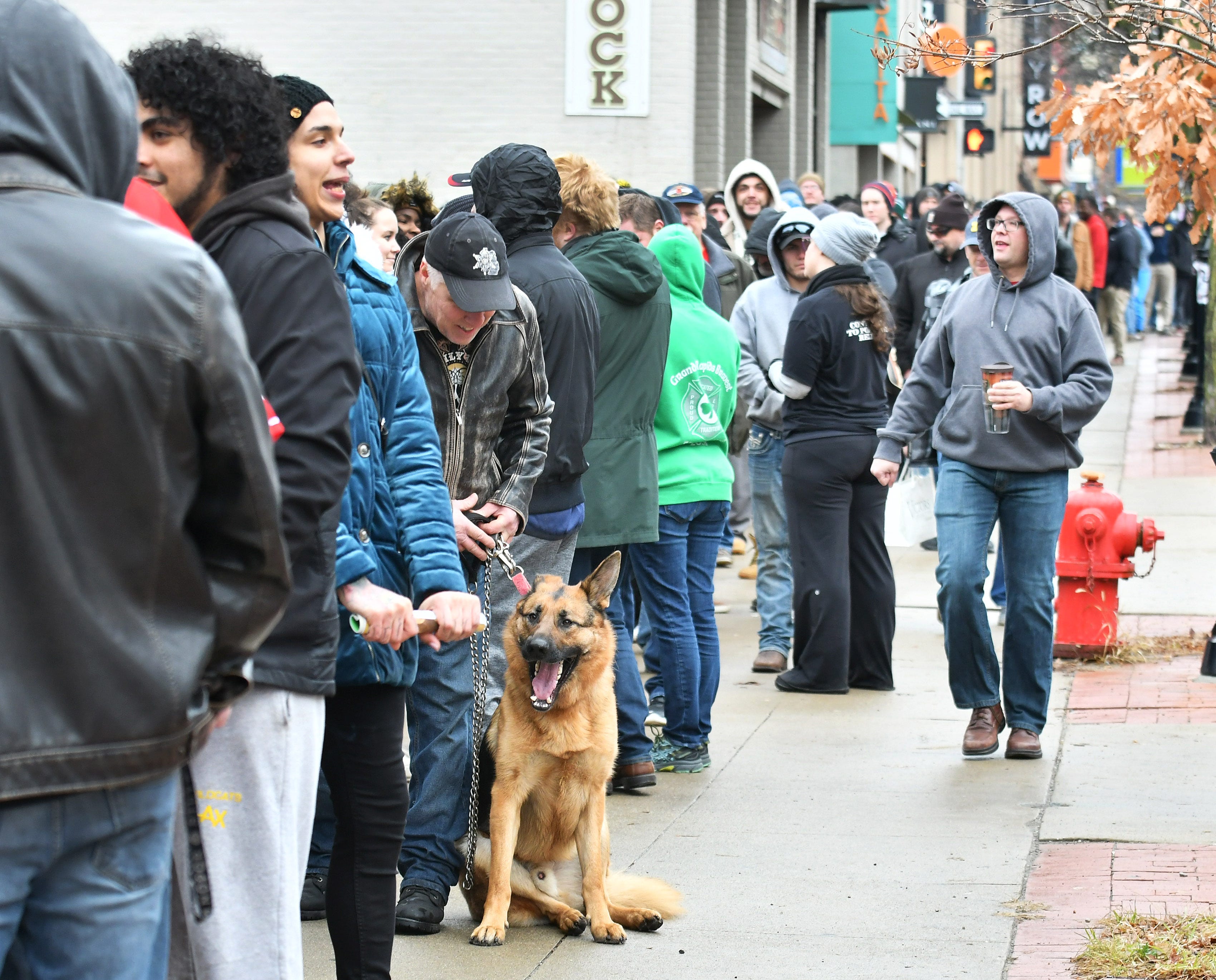 Kerry Dawe, 60, of Brighton, left, with his German shepherd, Otto, stands in a long line stretching about a block from Arbors Wellness.