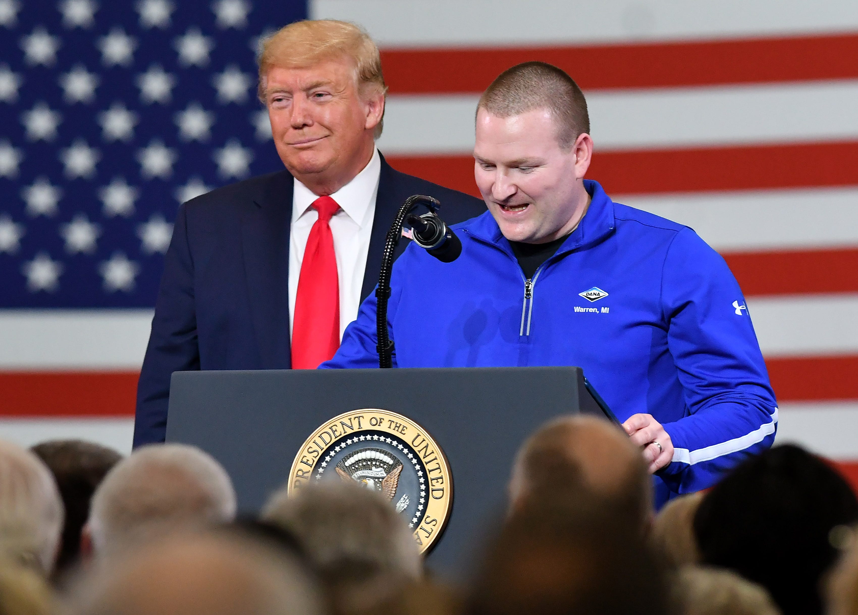 President Donald Trump listens while Dana Incorporated production supervisor and military veteran Devin Mallory, 34, of Washington Township, speaks after the President invited him on stage at Dana Incorporated in Warren, Mich. on Jan. 30, 2020.